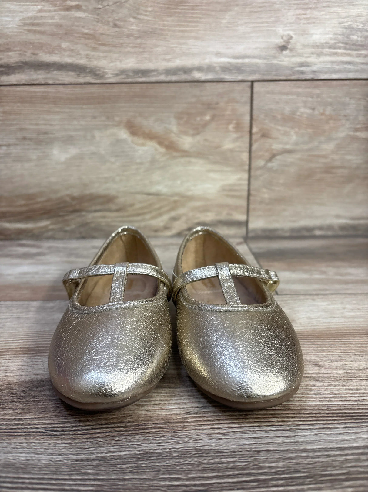 Front view of Susie T-strap ballet flats in metallic gold, size 8C, showing T-strap and rounded toe on wood background