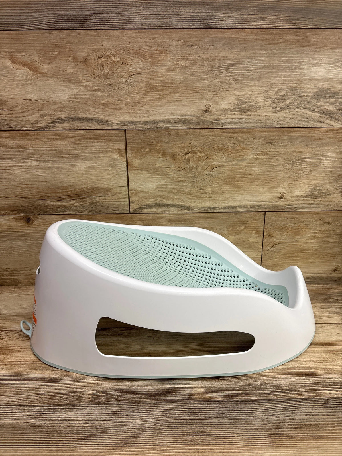 Side view of Angelcare Bath Support showcasing mint green perforated seat and white support frame on a wood surface
