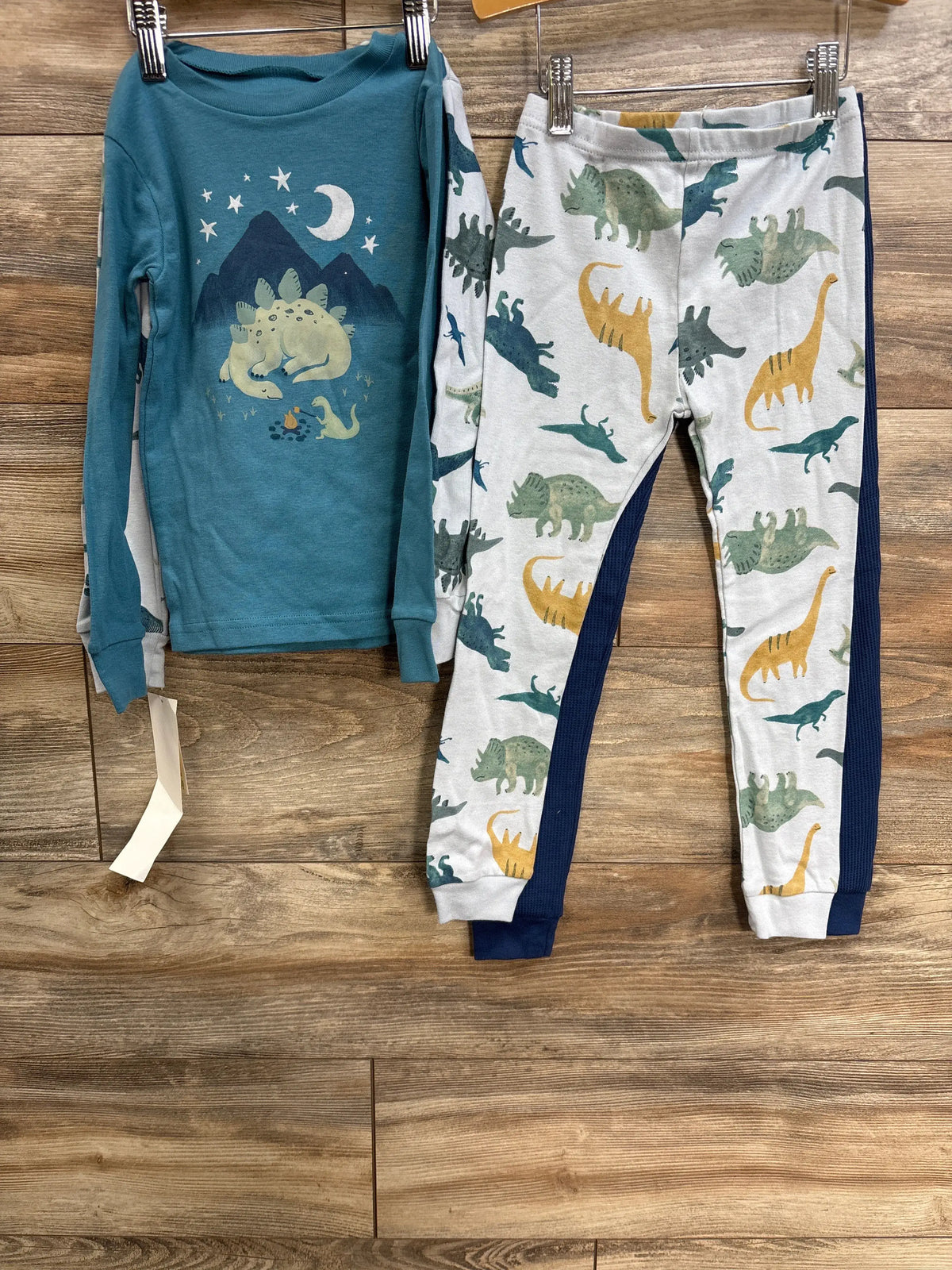 Front view of the white and grey Just One You 4T four-piece pajama set showcasing dinosaur prints on a wood floor