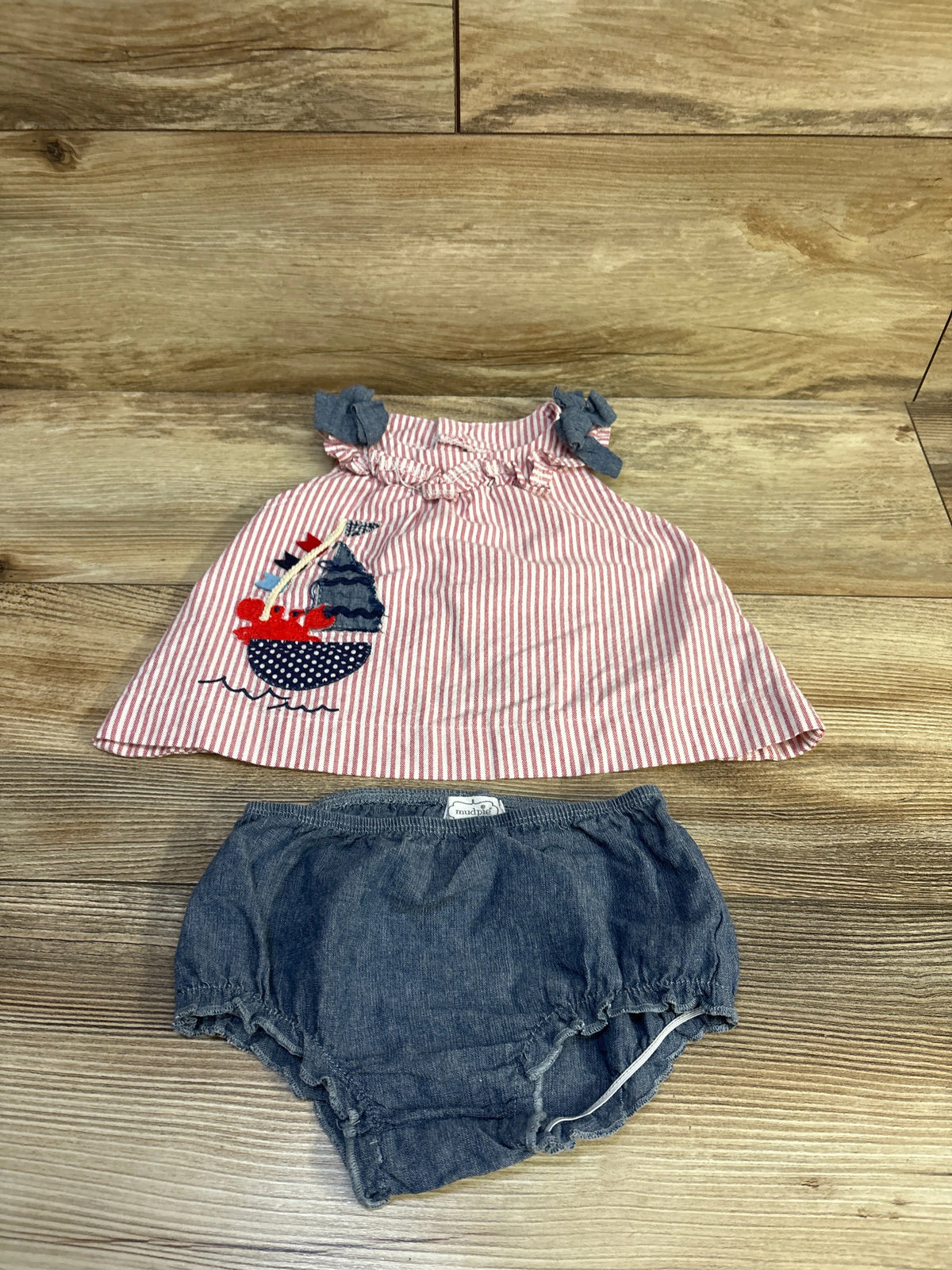 Flat lay of MudPie 2-piece top and shorts showing red-and-white striped ruffled top with sailboat applique and blue chambray bloomers on wood background
