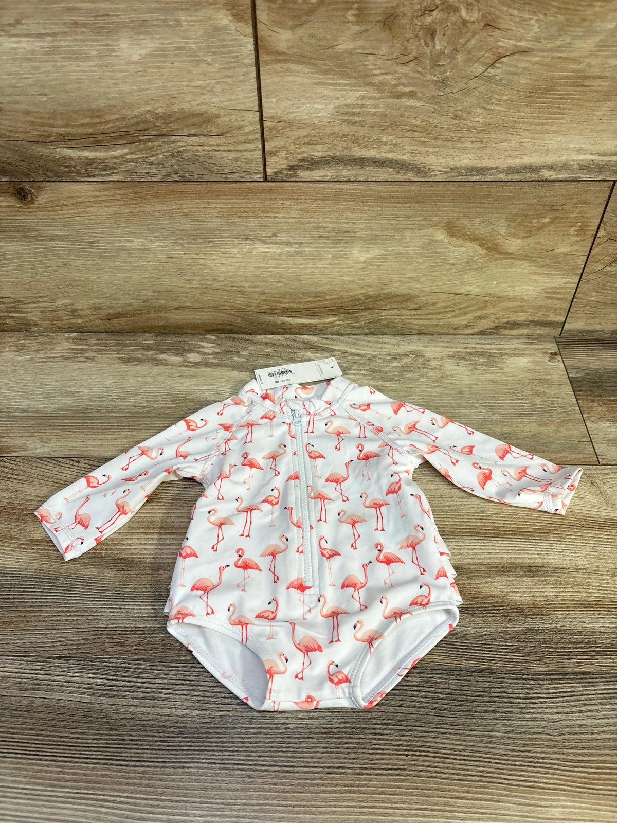 Front view of Janie & Jack white 0 to 3 month rash guard swimsuit showcasing flamingo print and half-zip on wood background