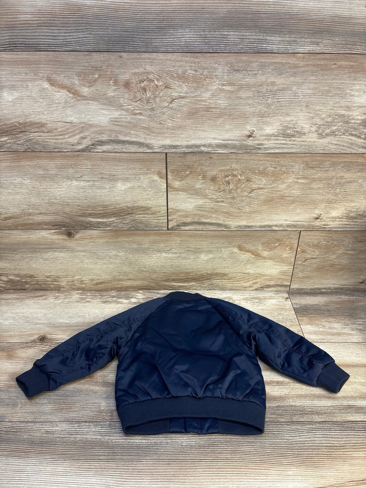 Navy blue kids bomber jacket with ribbed cuffs displayed on wood floor