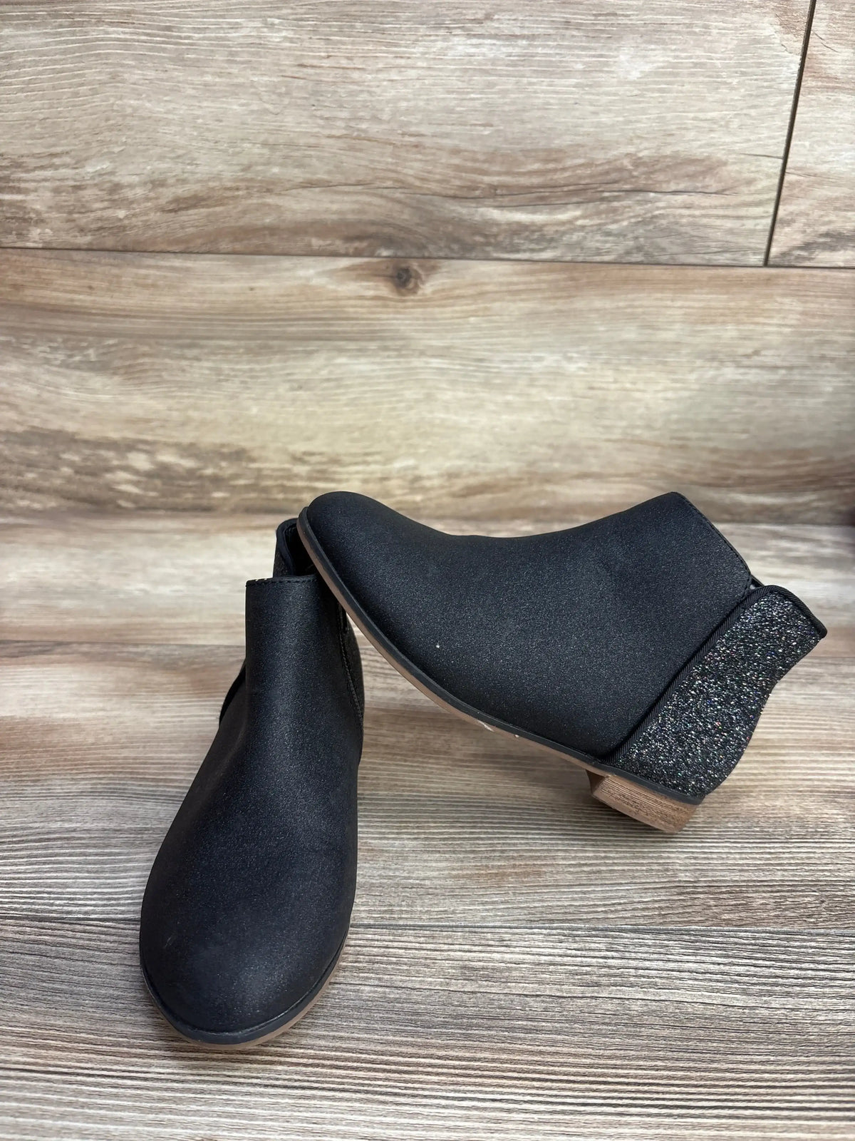 Side and front view of Cat & Jack black toddler ankle boots showcasing glitter heel panel and low stacked heel on wood floor