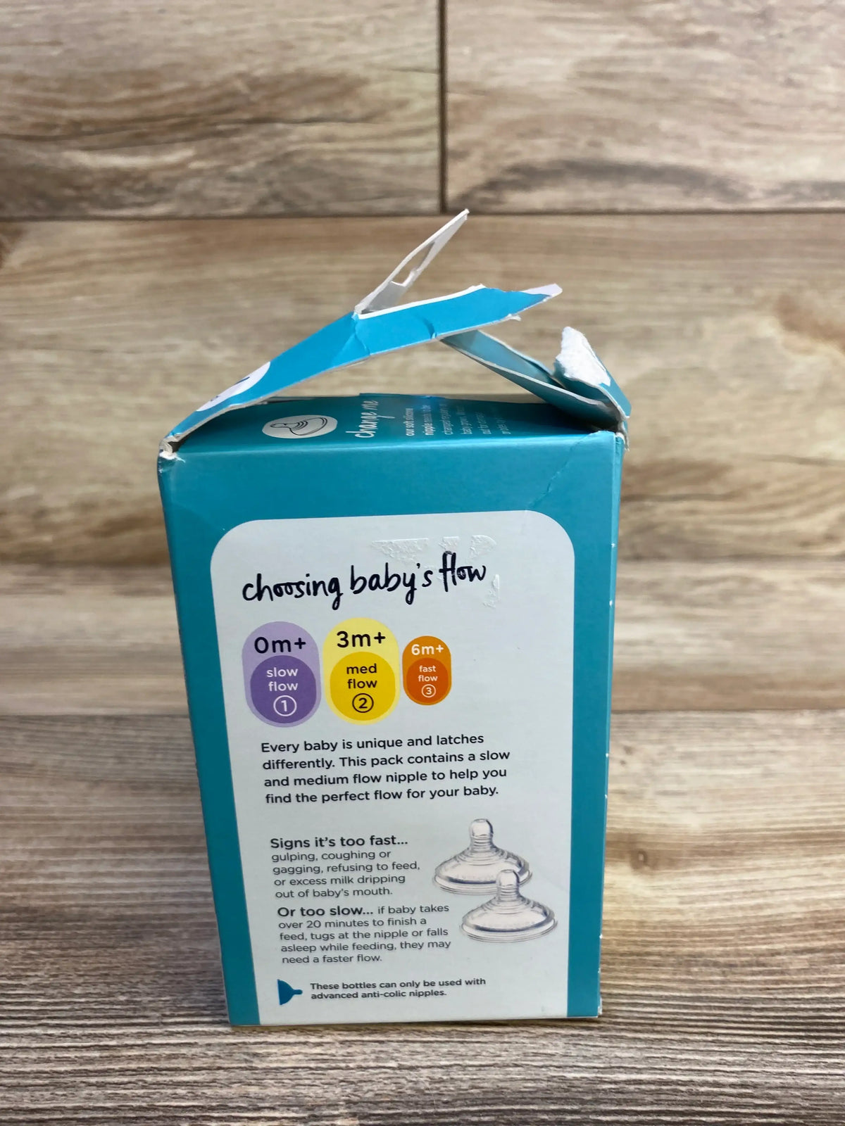 Side view of Tommee Tippee Advanced Anti-Colic 5oz bottle box showcasing choosing baby’s flow nipple guide and torn top on wood background