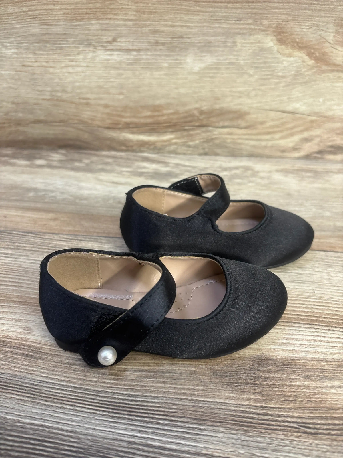Angled view of black FunkyMonkey Mary Jane ballet flats, size 6C, showcasing round toes and Velcro straps on a wood surface