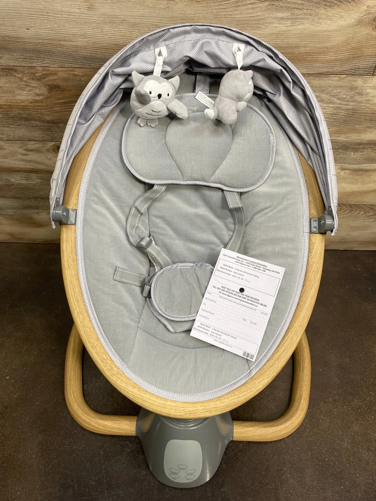 Gray baby bouncer with wooden frame, toy bar, padded seat, and plush hanging toys.