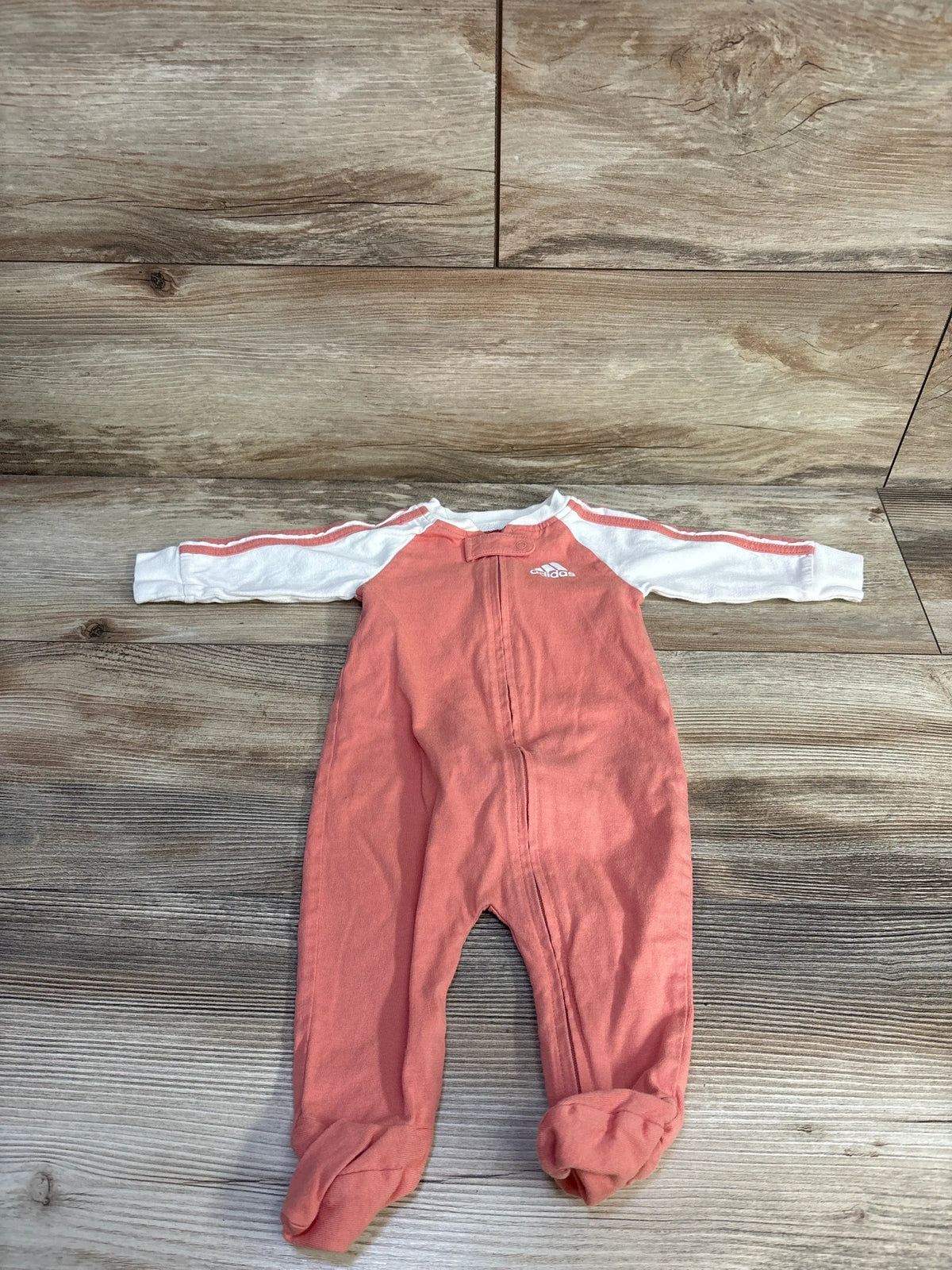 Front view of Adidas coral baby sleeper in size 3 months showcasing long sleeves, footed legs, and front zipper on a wood-look floor