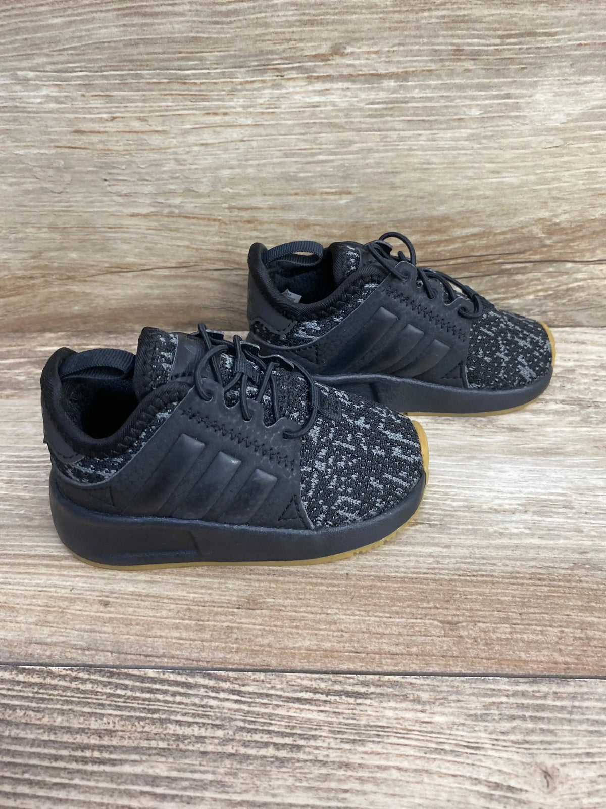 Angled side view of Adidas X_PLR toddler sneakers size 4C in black, knit upper and gum-textured sole on wood background