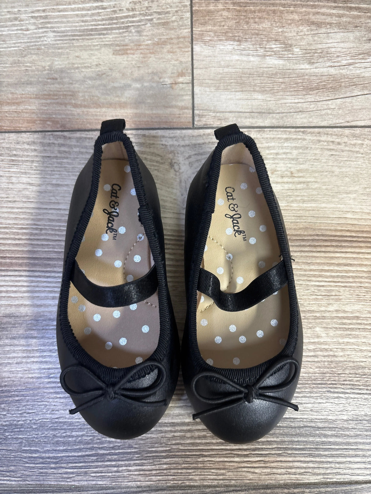 Top down view of Cat and Jack ballet flats in black with elastic strap, bow detail and polka dot insole on wood floor