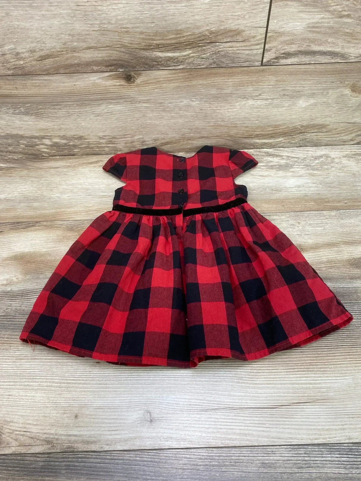 Flat lay of red and black buffalo-check cap-sleeve toddler dress (2T) showing button-front bodice, velvet waist trim on wood floor