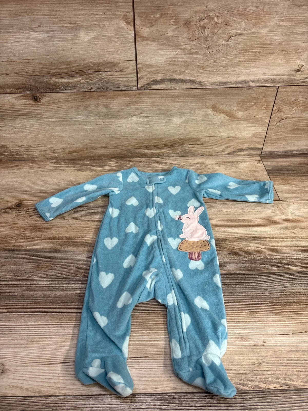 Blue baby sleeper with white heart pattern and bunny patch, footed, laid on wood floor