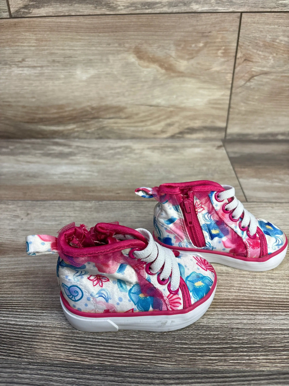 Three-quarter view of toddler pink Disney floral high-top sneakers showing side zipper, white laces, and white rubber sole on wood floor