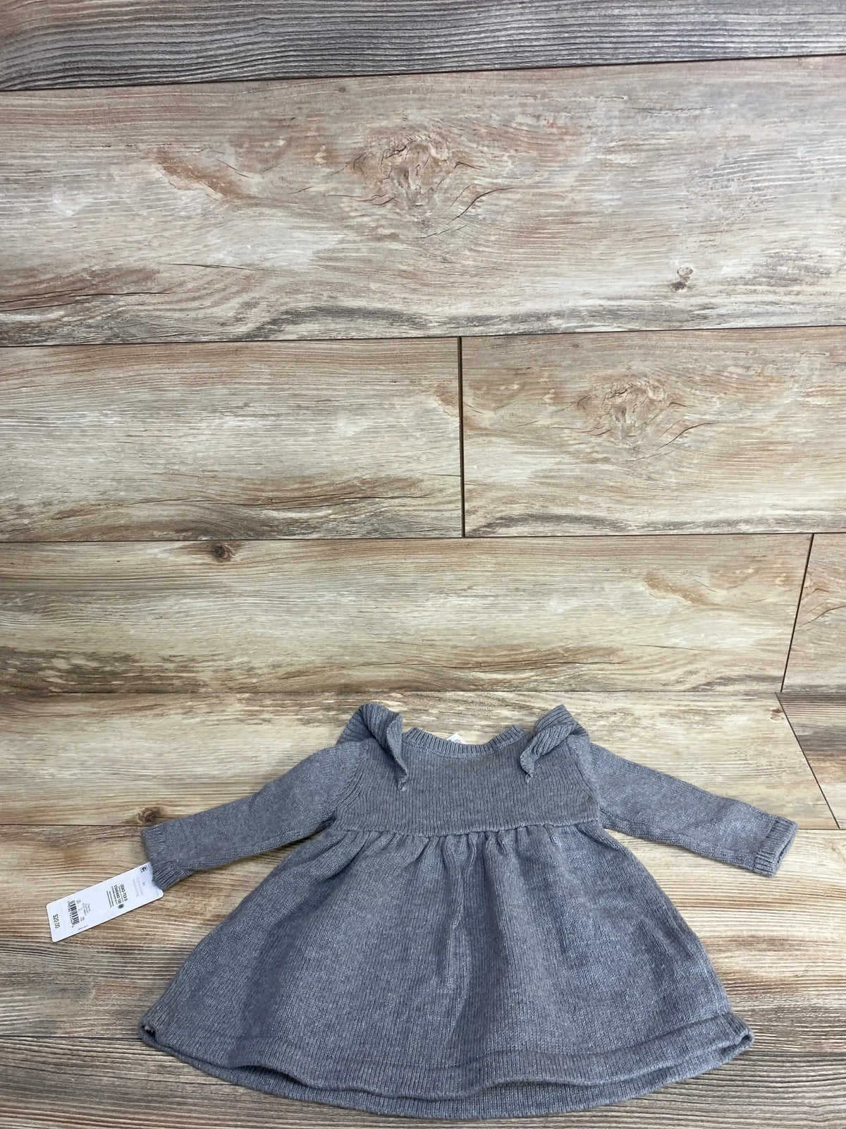 Gray knit baby dress with long sleeves and bow accents on wooden background