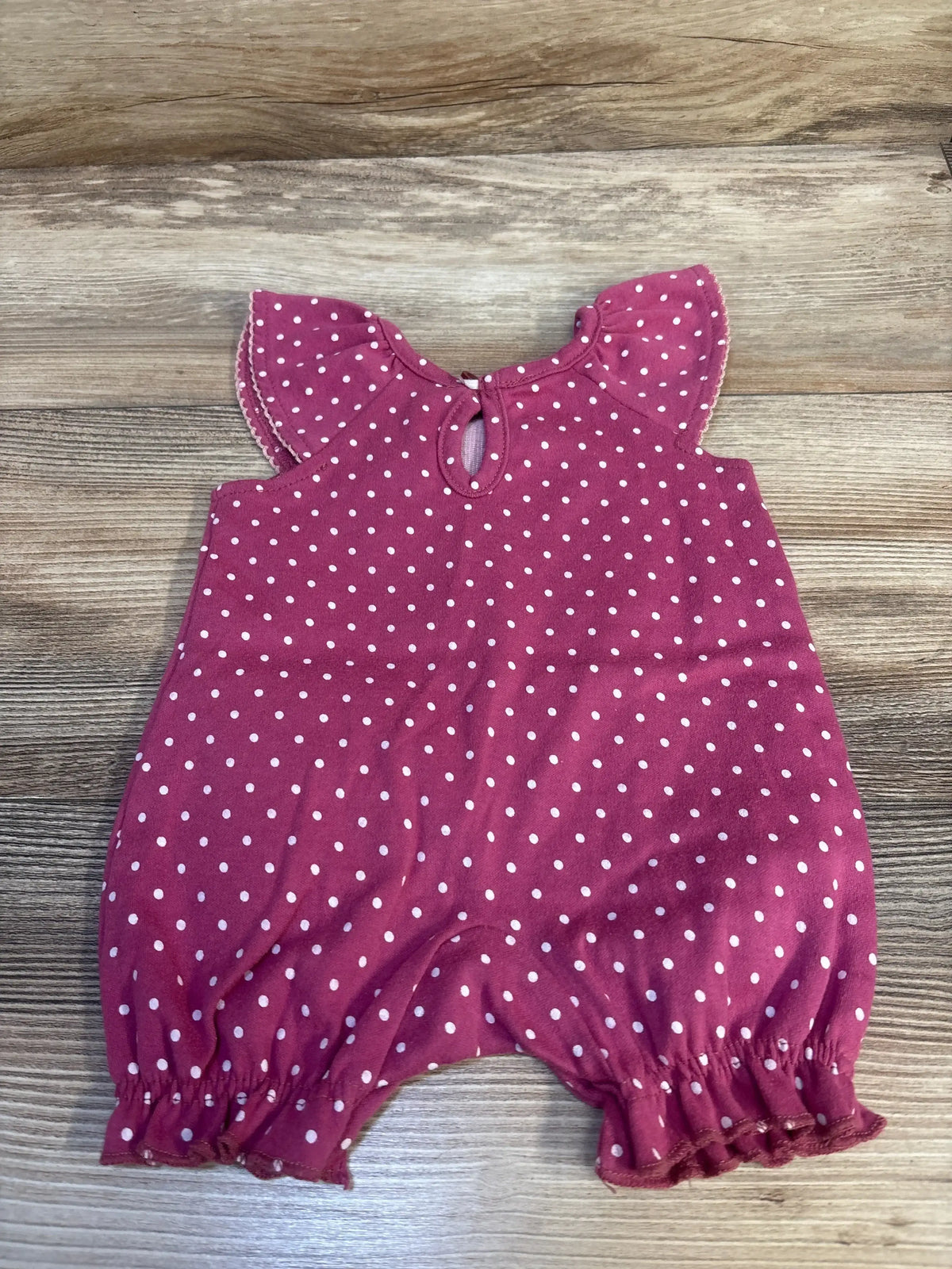 Front flat lay of mauve polka dot shortie romper with flutter sleeves, keyhole back and elasticized leg openings on wood
