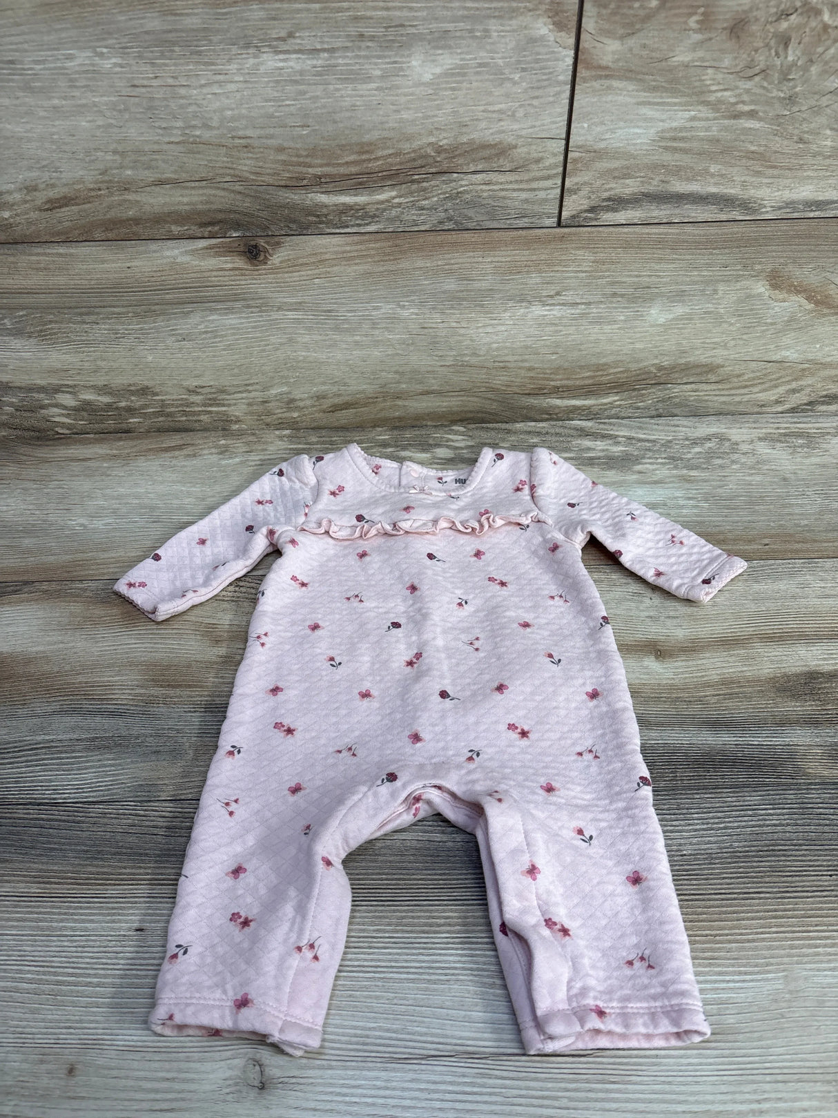 Pink quilted baby romper with long sleeves and small floral print on wooden floor