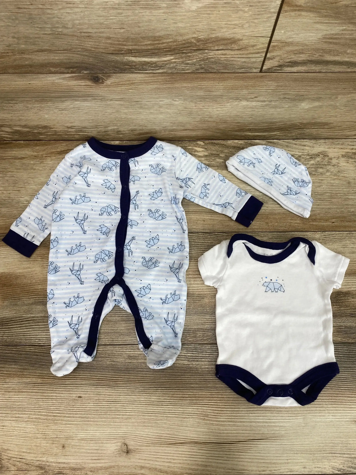 Flat lay of 3-piece animal-print baby sleeper set showing blue footed sleeper, white bodysuit, and matching hat on wood background