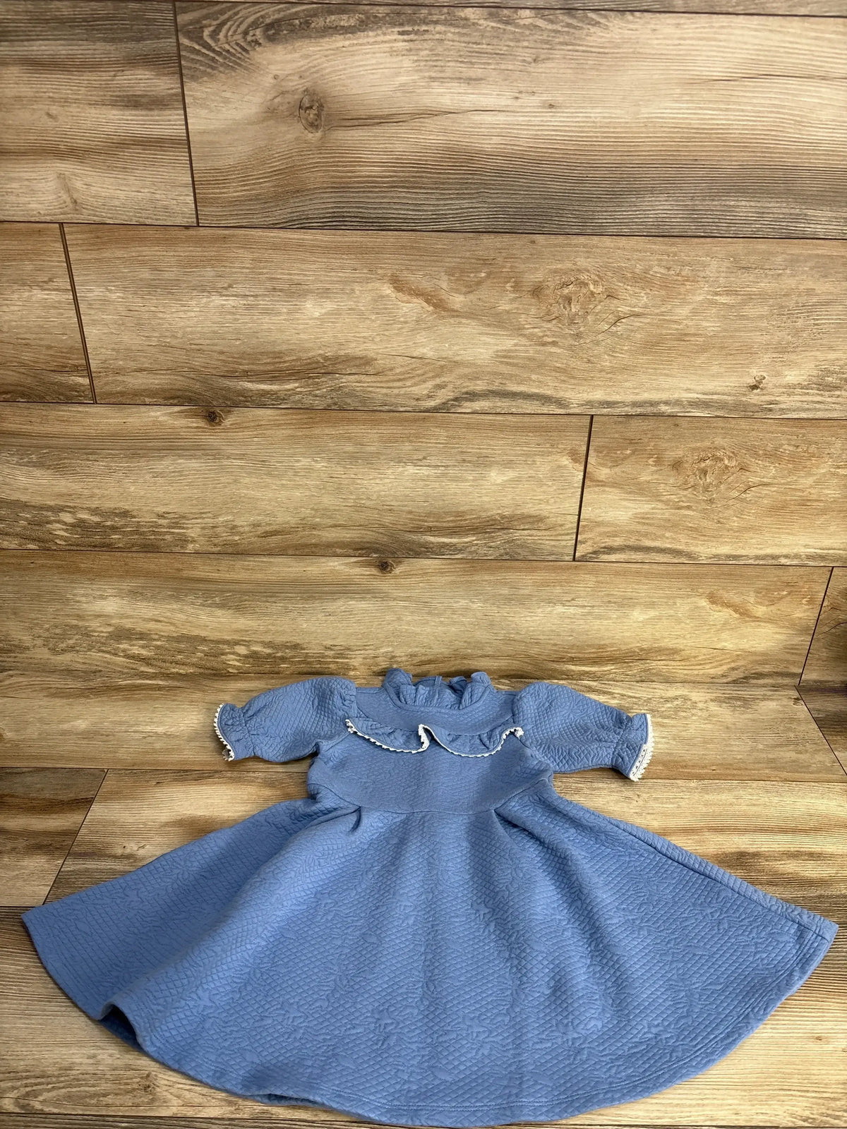 Flat lay of Janie and Jack pale blue jacquard dress size 3T showing ruffled collar and lace trim on wood floor