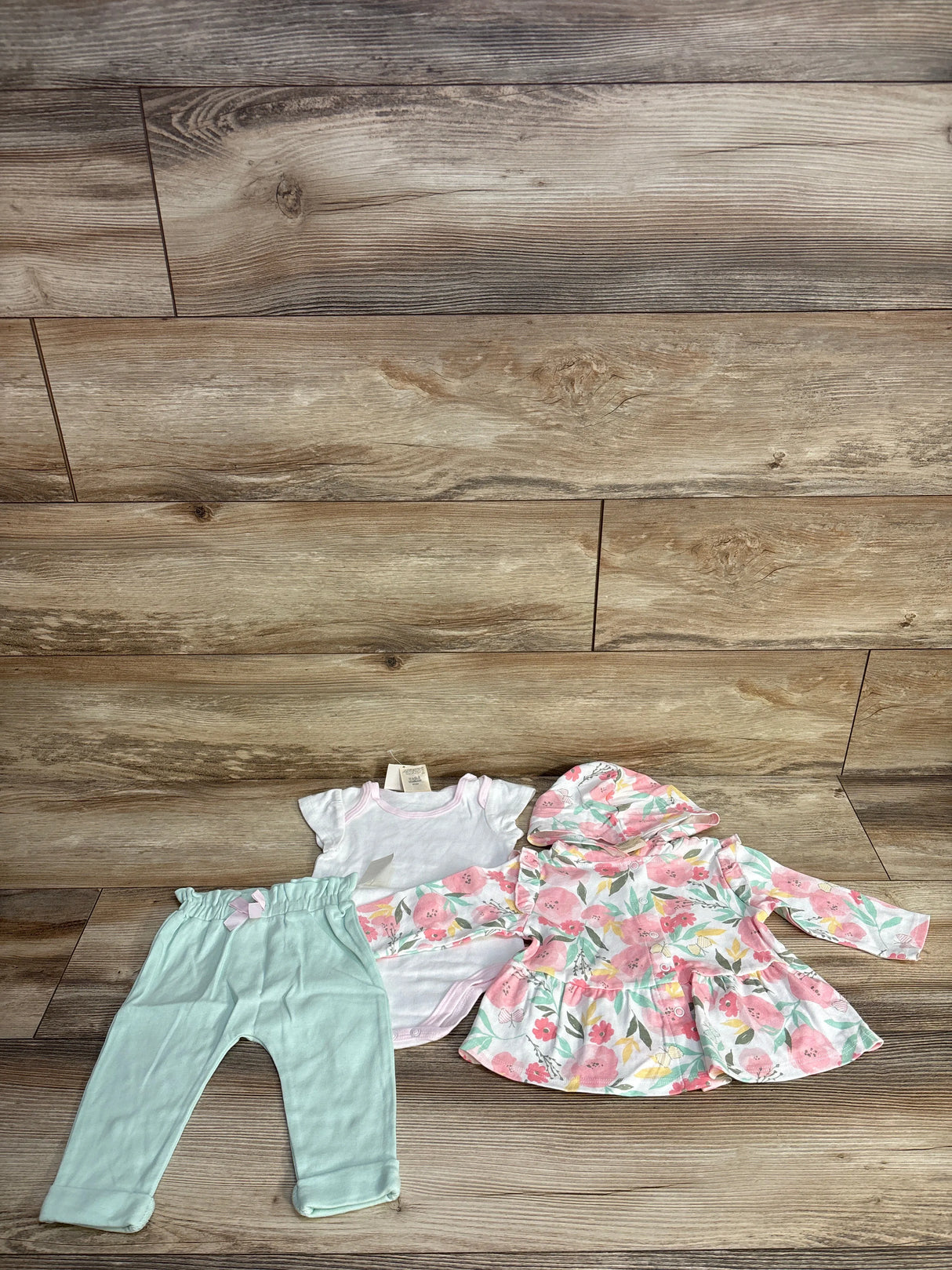 Floral baby outfit set with mint pants, white onesie, and pink floral hooded jacket on wood floor