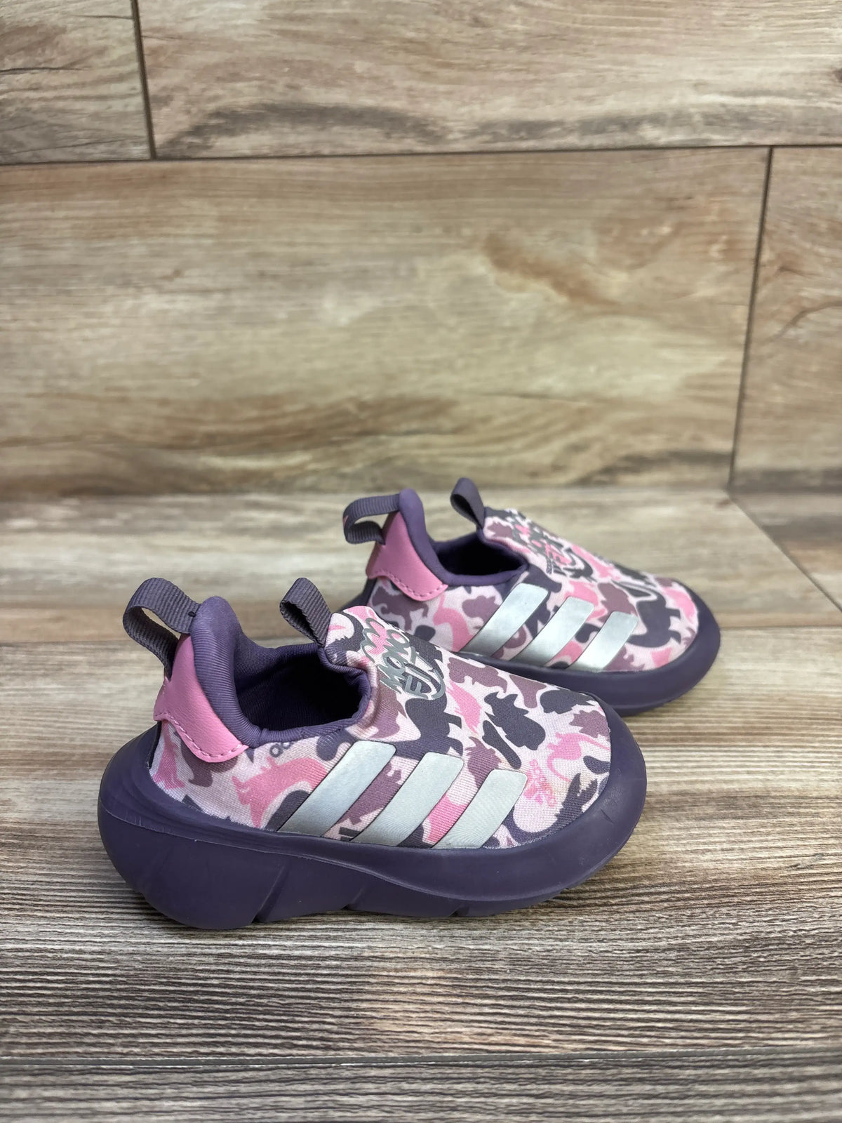 Three-quarter view of Adidas MonoFit slip-on sneakers with pink and purple camouflage uppers, white stripes, and pull tabs