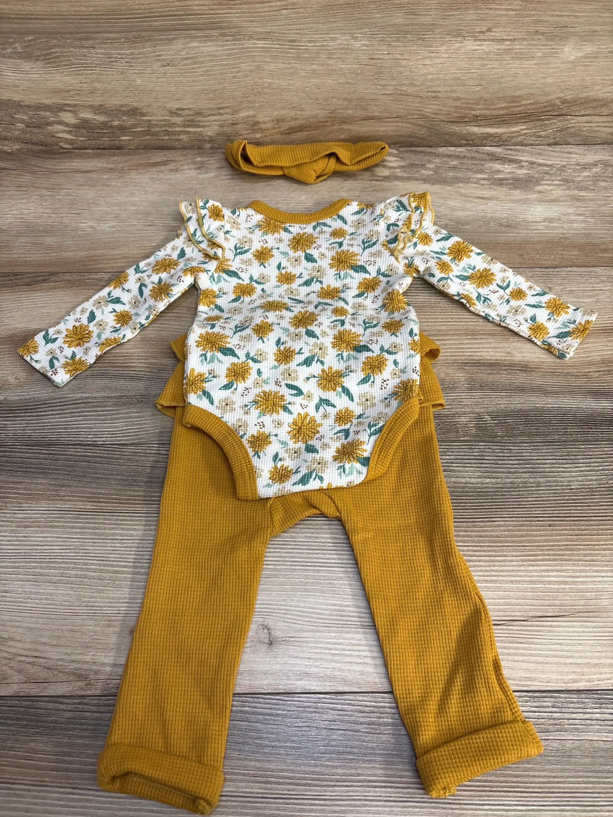 Flat lay of 3-piece waffle bodysuit set with floral long-sleeve bodysuit, mustard pants, and headband on wood