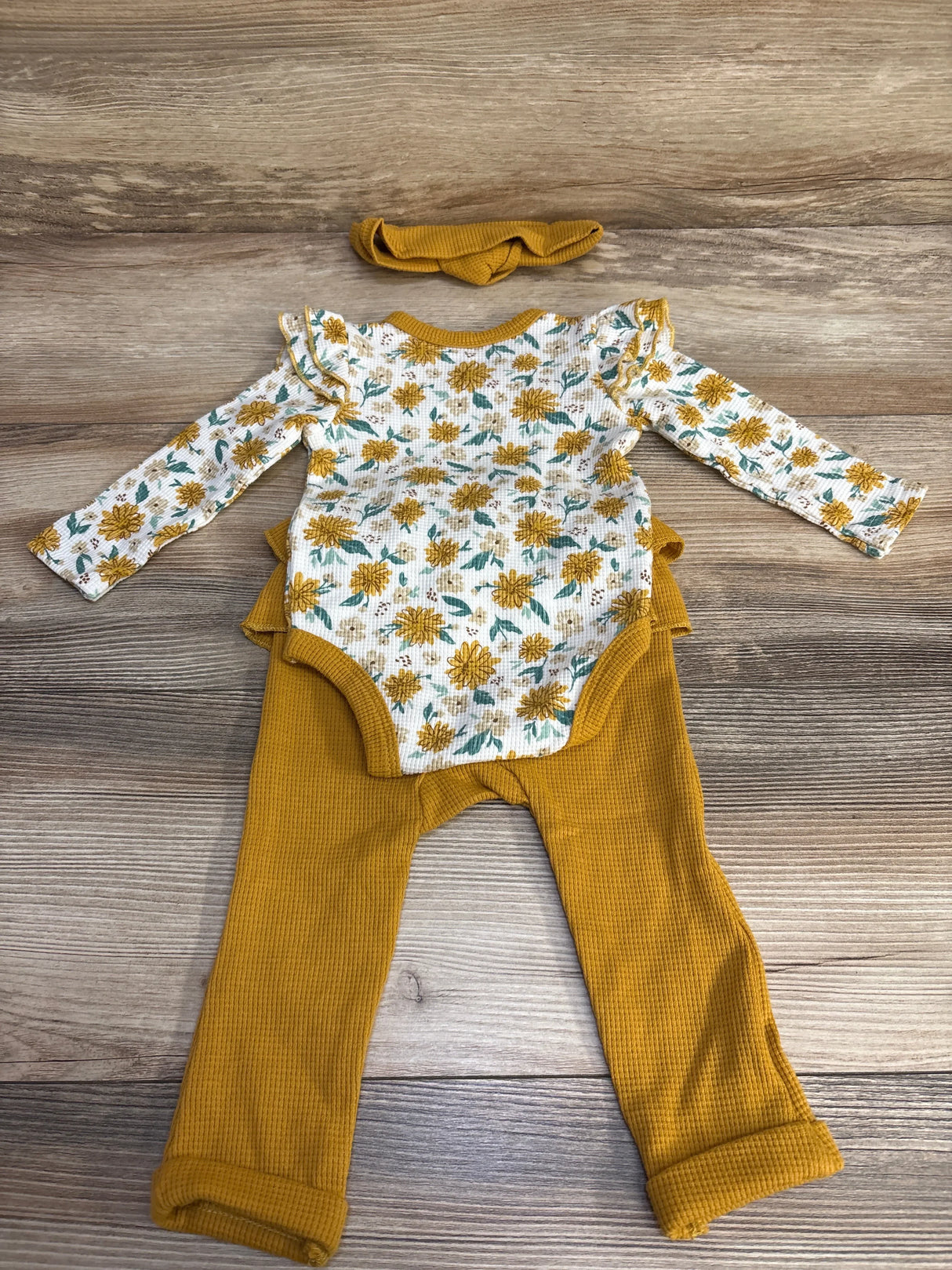 Flat lay of 3-piece waffle bodysuit set with floral long-sleeve bodysuit, mustard pants, and headband on wood