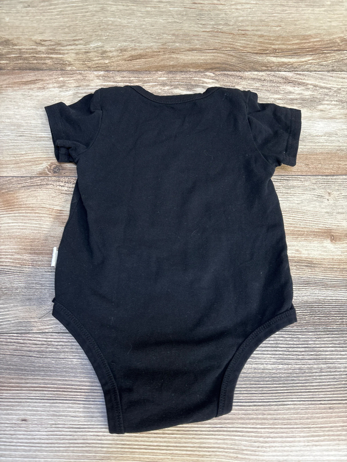 Black baby onesie with ruffled short sleeves on wood floor, kids clothing resale