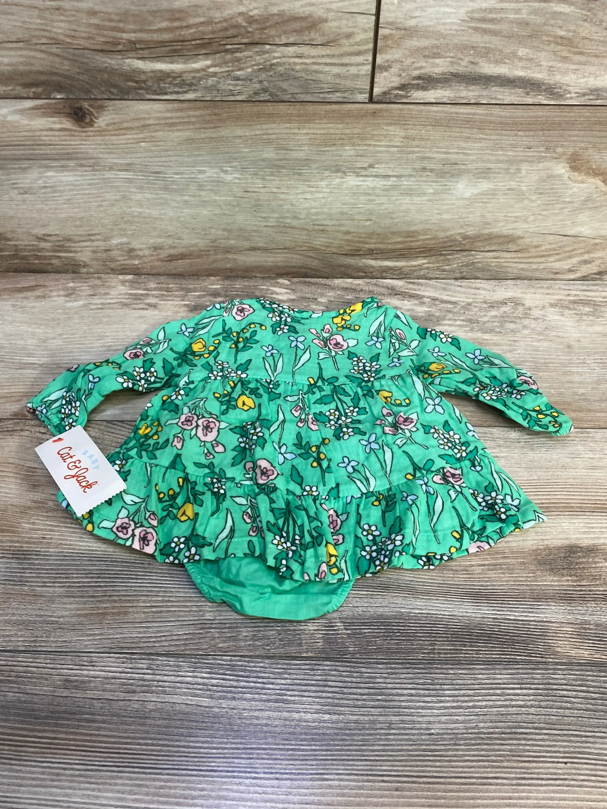 Back view of NEW Cat and Jack Floral Henley Dress and Bloomers in green showcasing multicolor floral print with ruffle hem and brand hangtag on wood plank floor