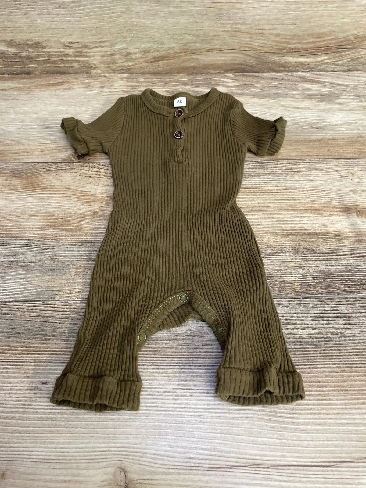 Flat-lay of green ribbed Henley baby romper showing two-button placket, snap crotch and ruffle leg cuffs on light wood background