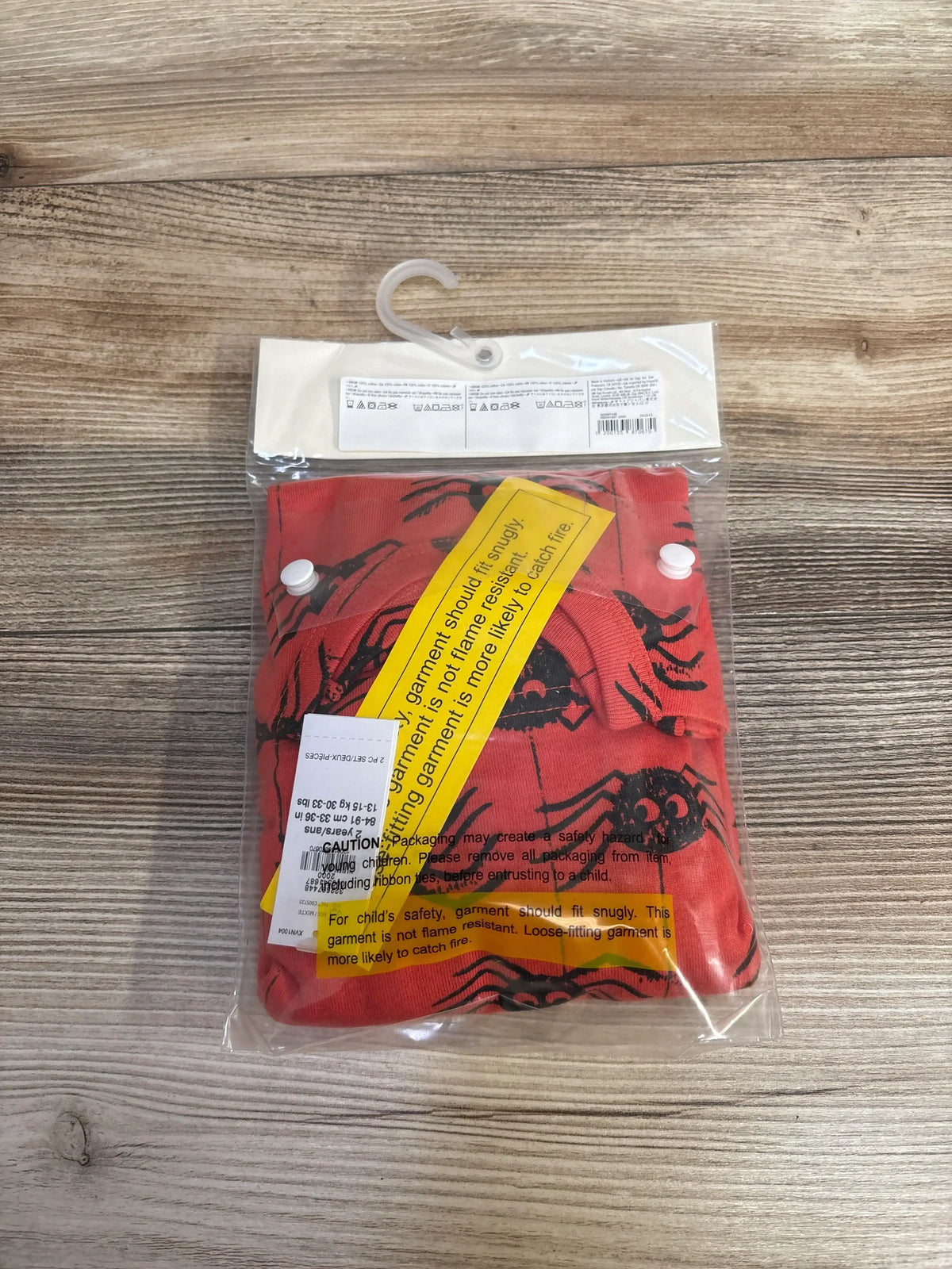 Top view of 2T Baby Gap organic two-piece orange pajama set showcasing black spider print and yellow safety labels on wood background