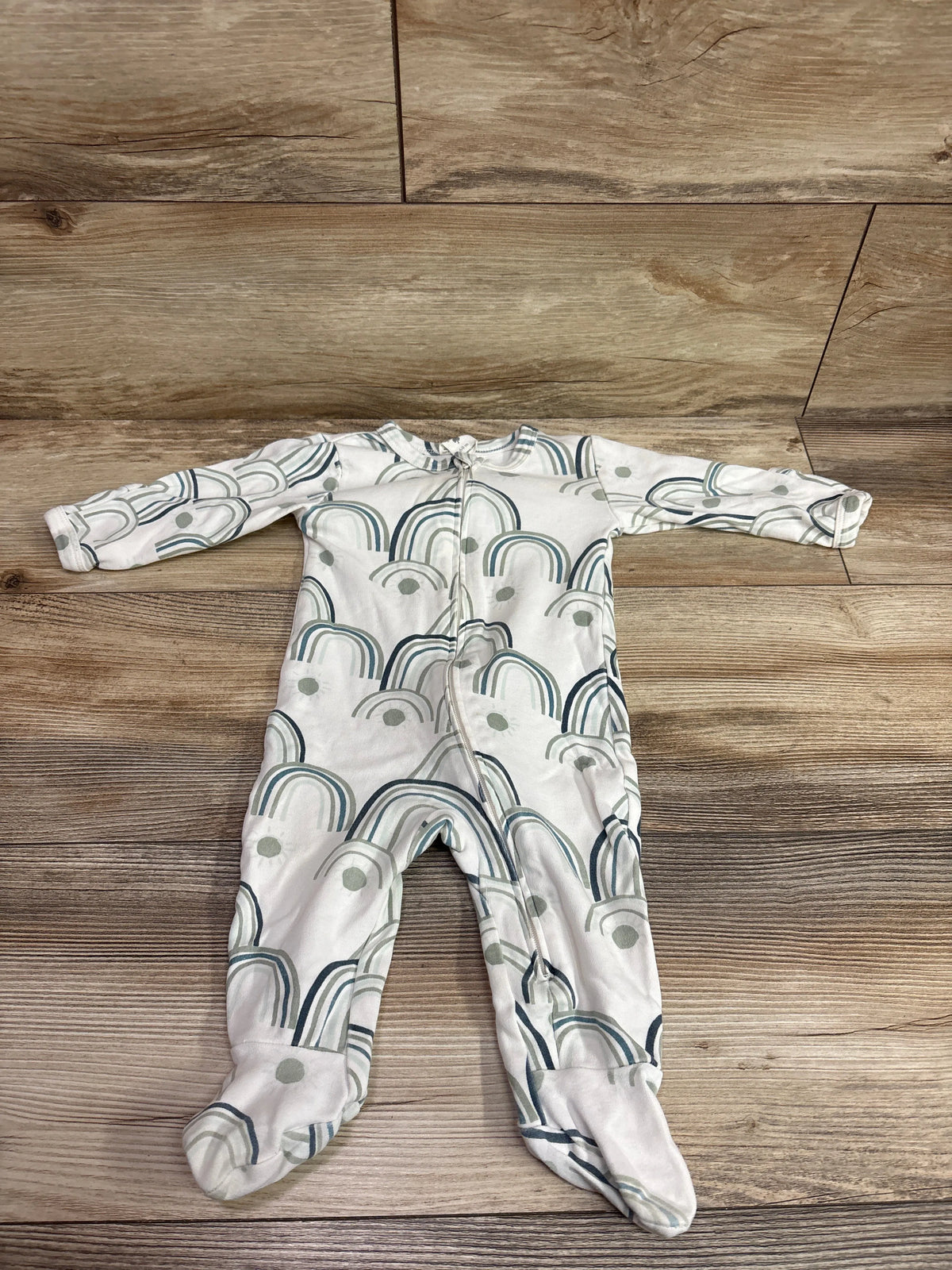 White Kate Quinn organic footie sleeper with blue and green rainbow print on a wood background