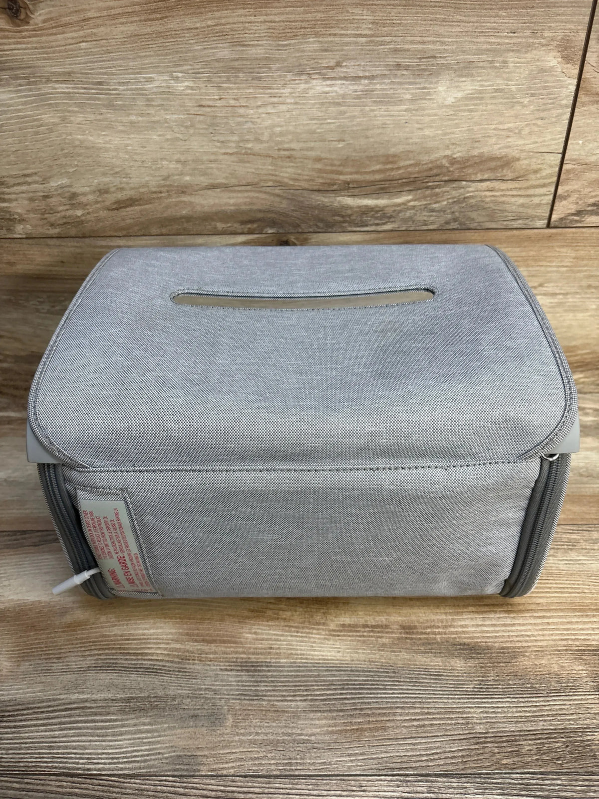 Front-top view of Munchkin 59S UV Cleaning Bag showing gray fabric exterior, top carry slot, side USB cable and zipper on wooden background