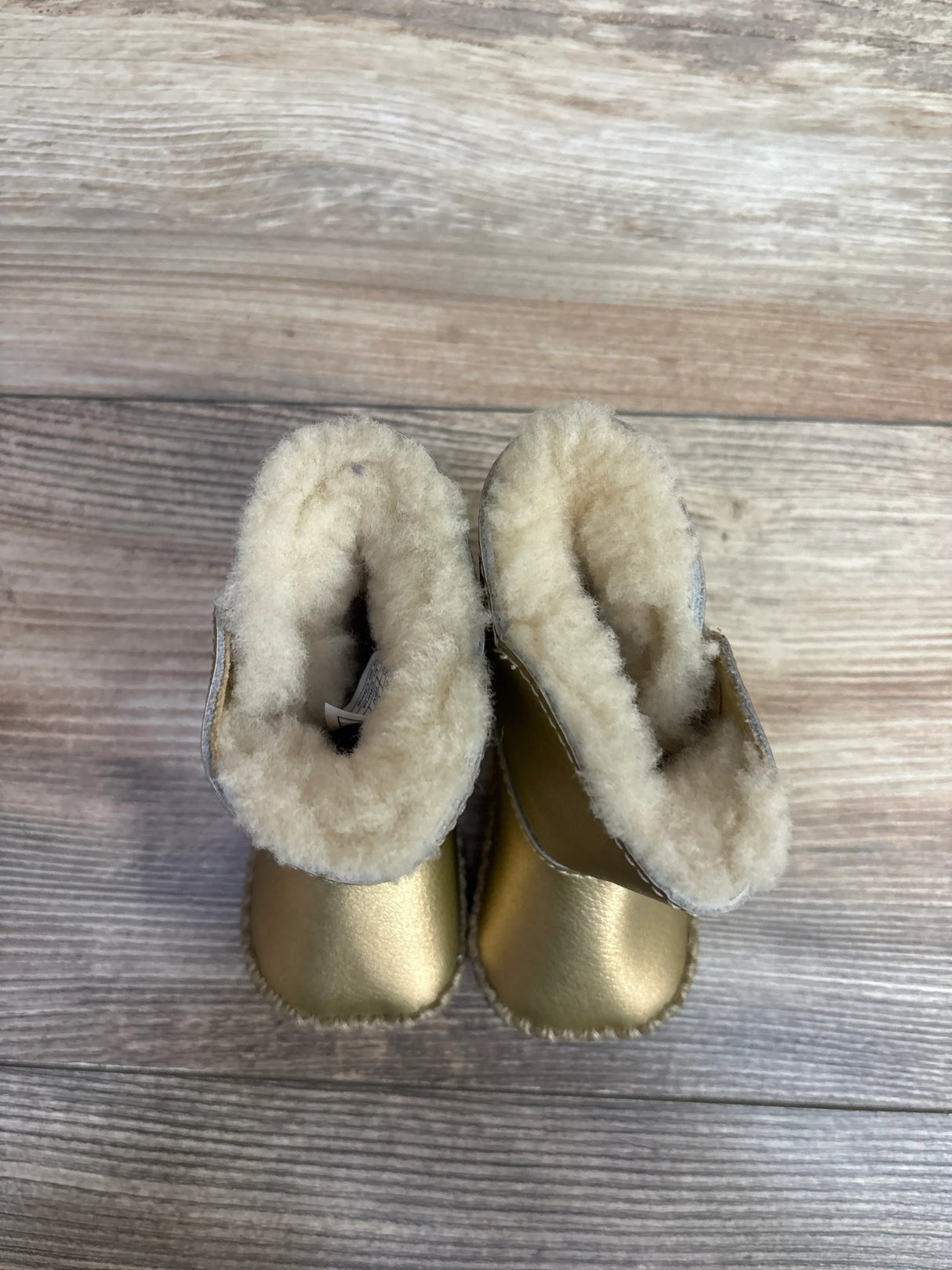 Top view of cozy gold baby boots with fluffy cream lining on wooden floor