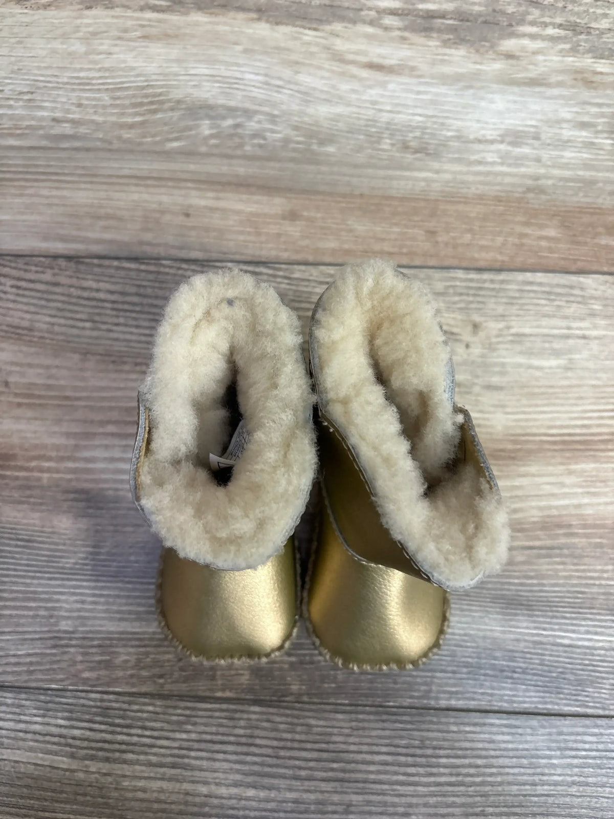 Top view of cozy gold baby boots with fluffy cream lining on wooden floor