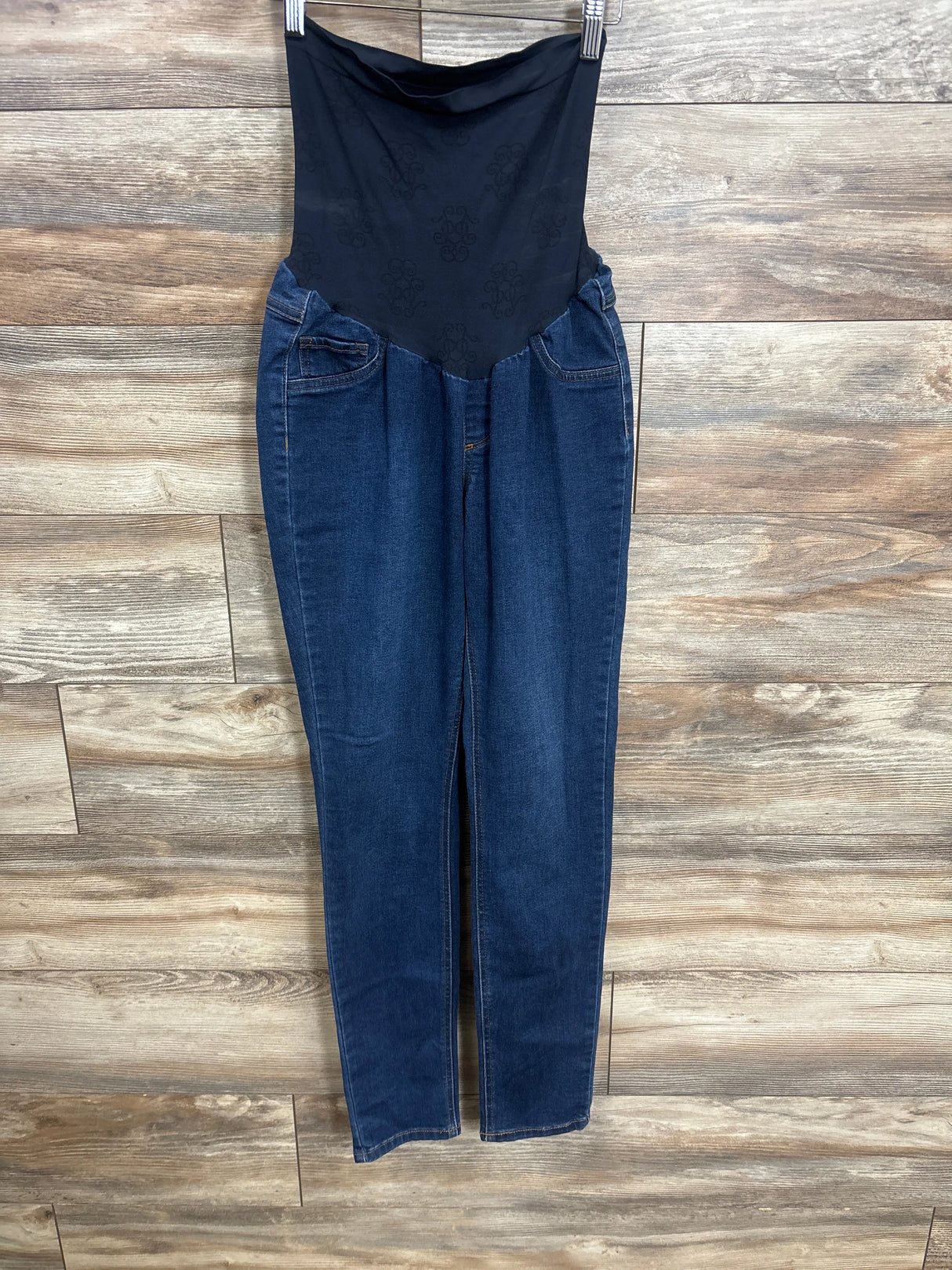 Dark blue maternity jeans with stretchy black waistband hanging against wood plank background