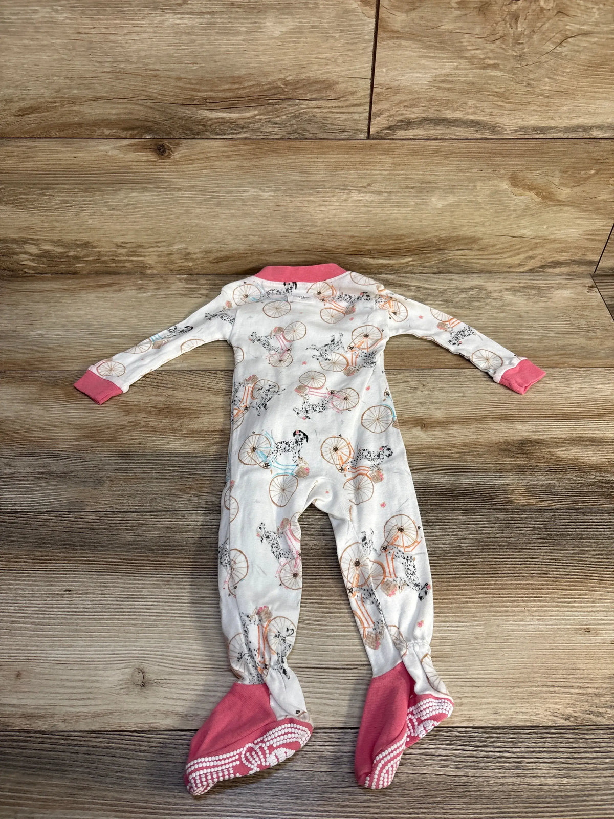 Front view of Burt’s Bees Baby organic sleeper showcasing bicycle and dog print, pink cuffs and footies, on a wood floor