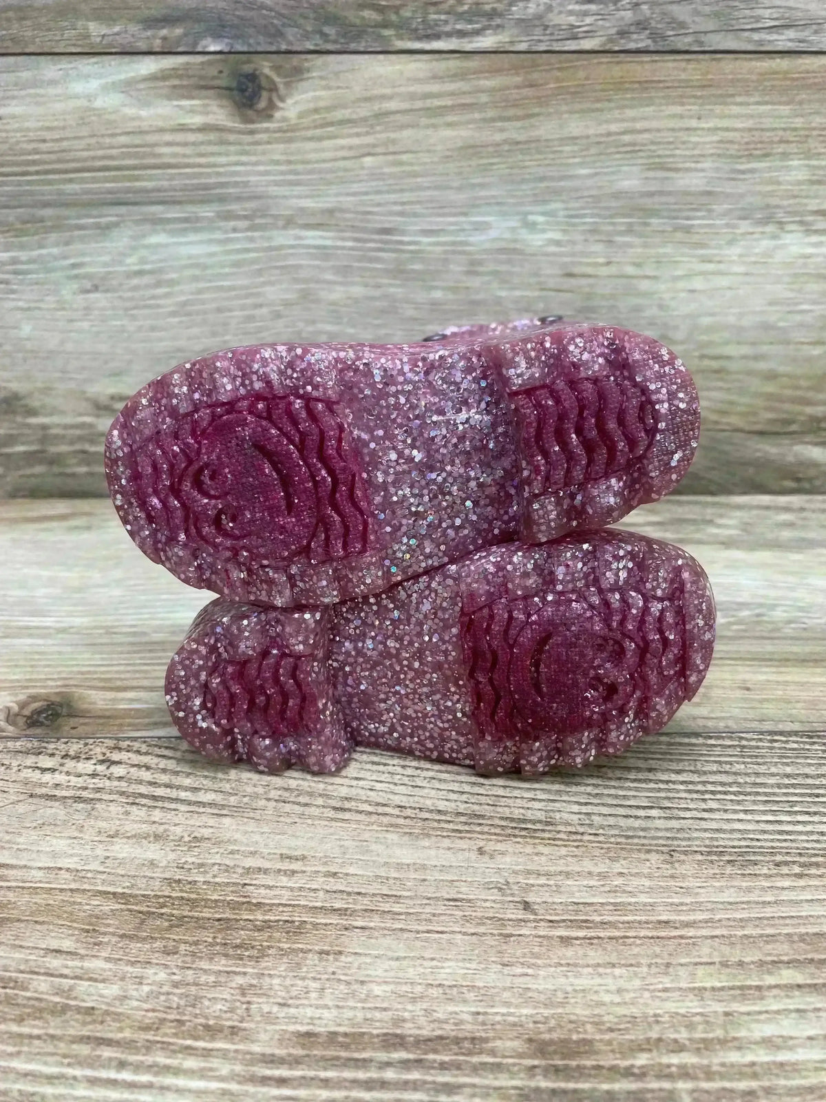 Close-up of Western Chief pink glitter light-up rain boot soles showing glitter finish and smiley tread on wood background