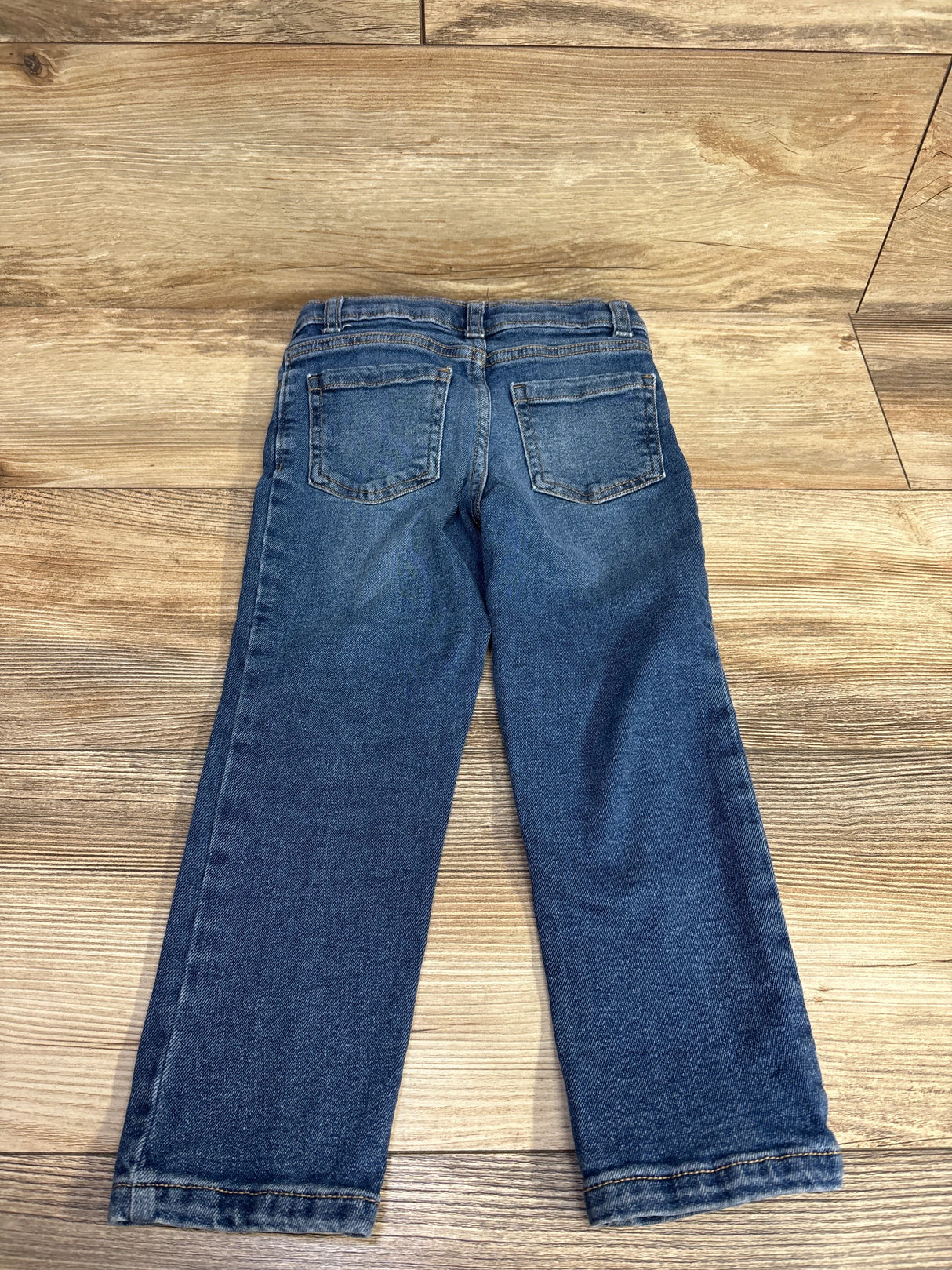Children's blue denim jeans with back pockets on wooden floor background