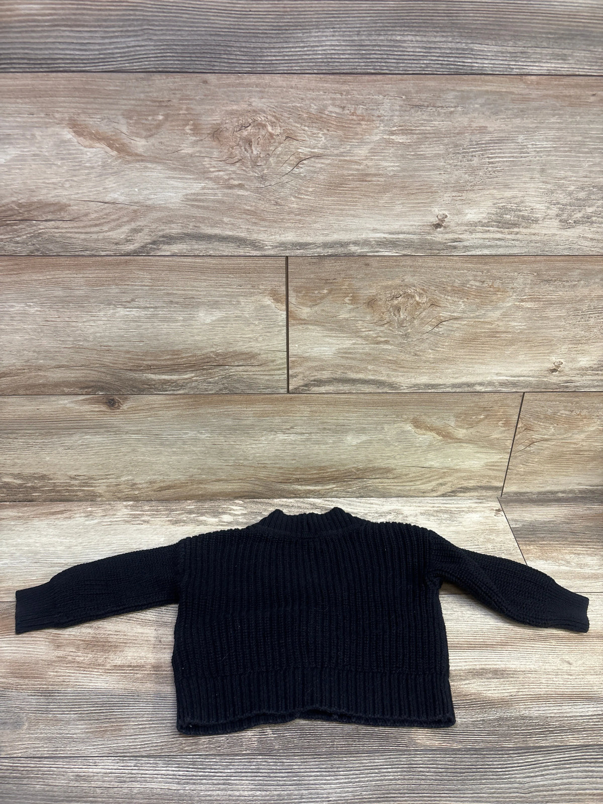 Front view of Baby Gap black knit button up cardigan in size 12 to 18 months showcasing ribbed texture on a wood look floor
