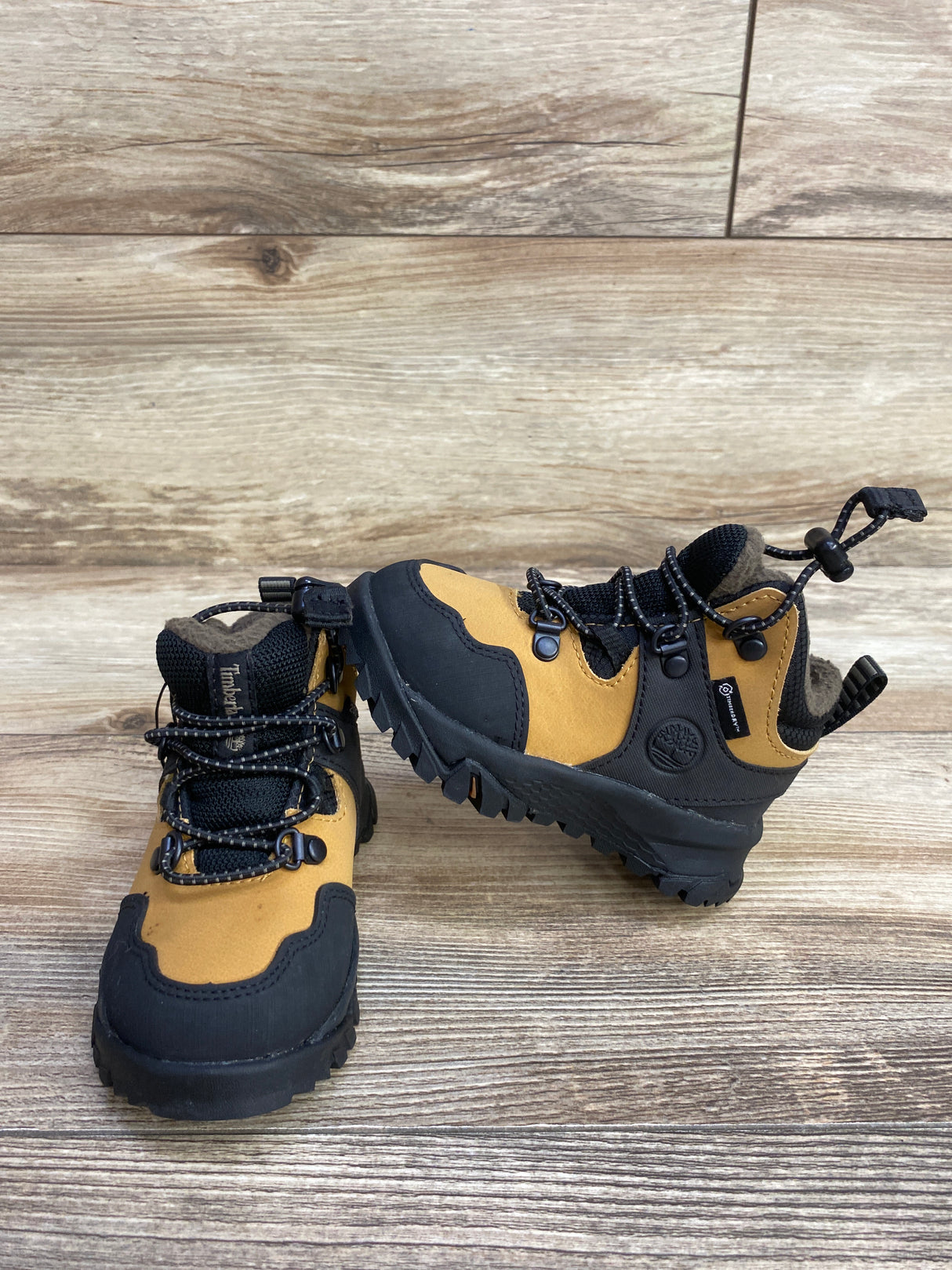 Pair of tan and black Timberland kids hiking boots on wooden floor background