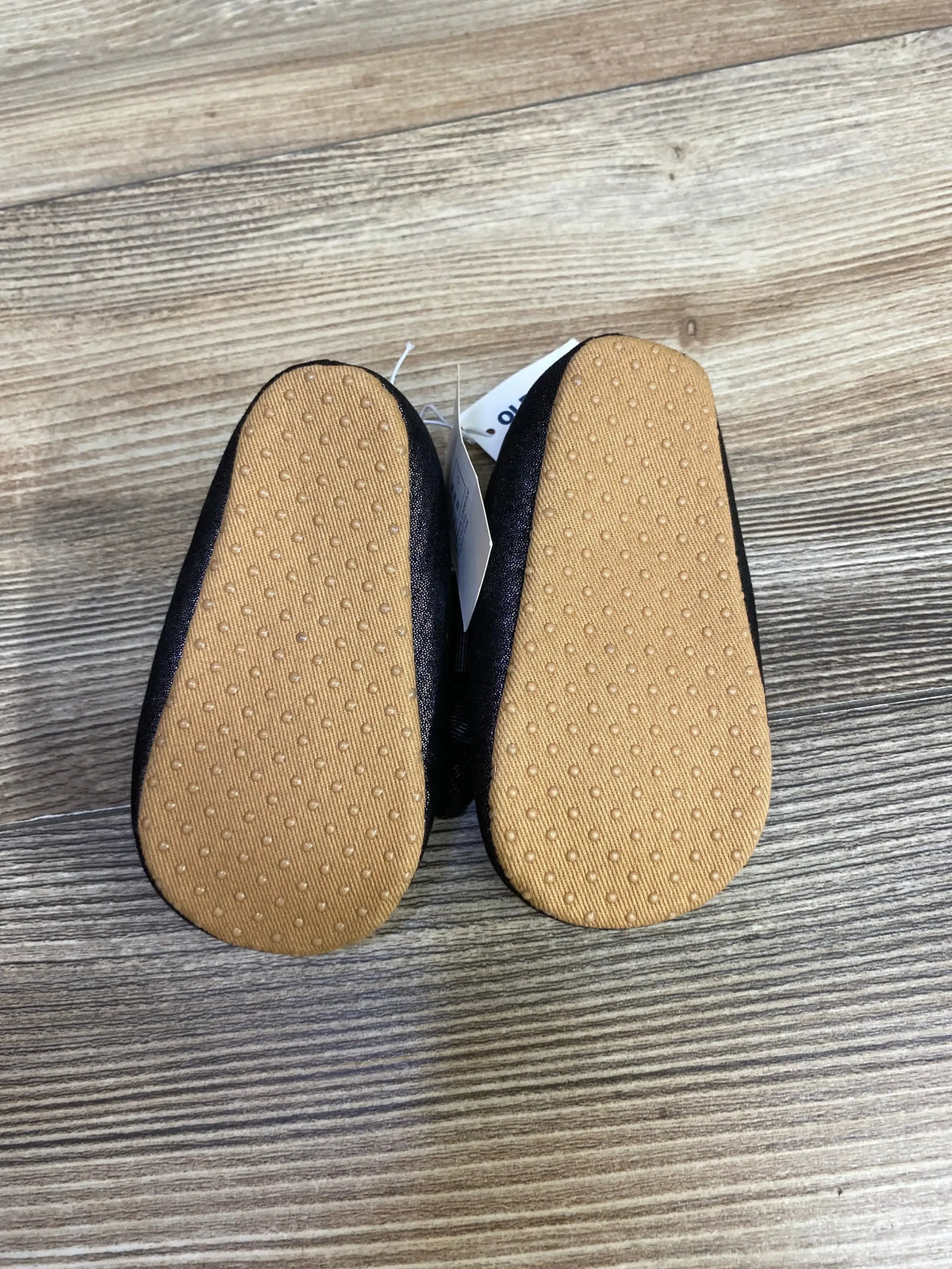 Bottom view of black baby shoes with textured brown soles on wooden surface