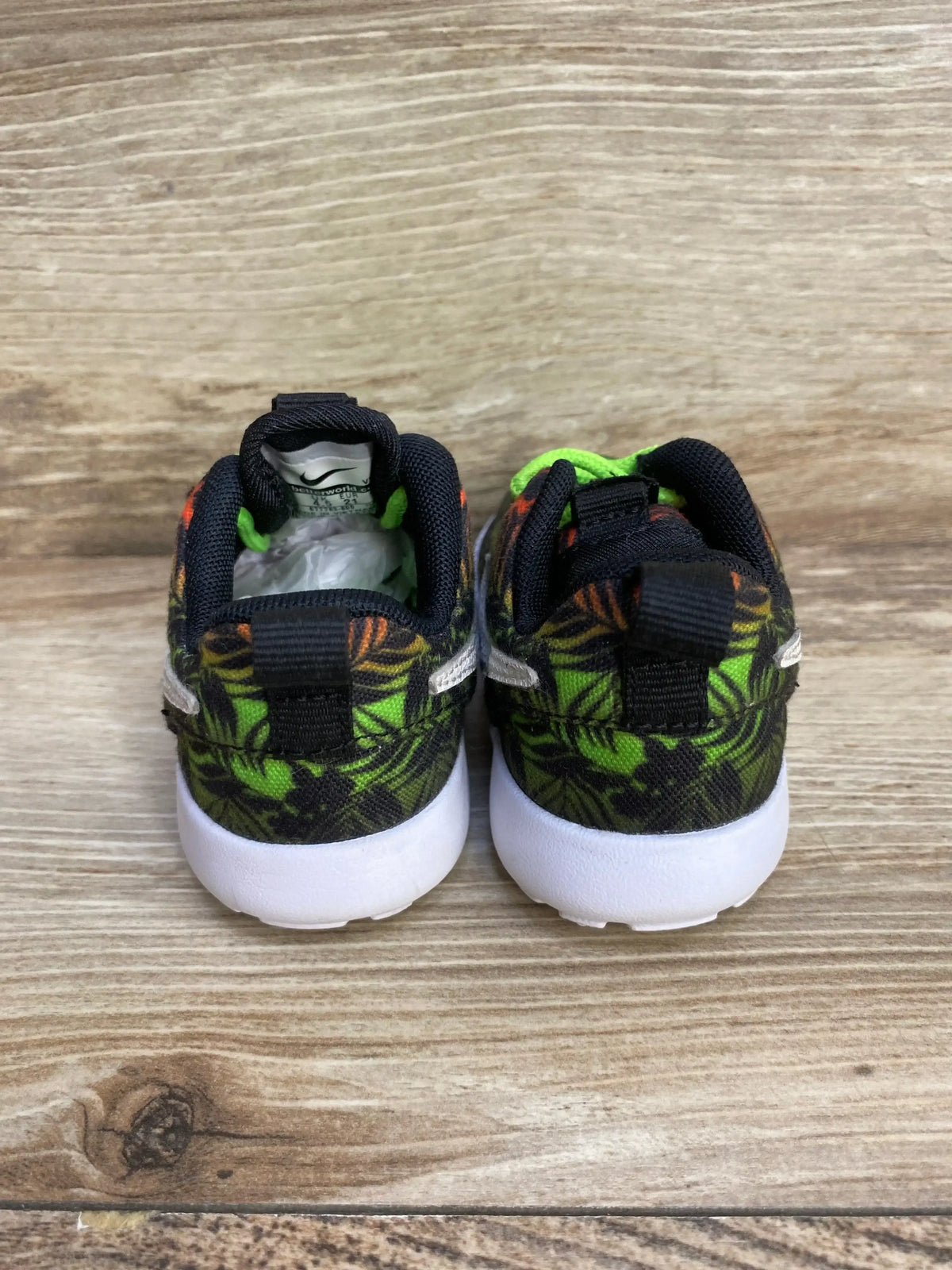 Rear view of Nike Roshe Run toddler sneakers, size 5C, green and black tropical print with white soles on wood background