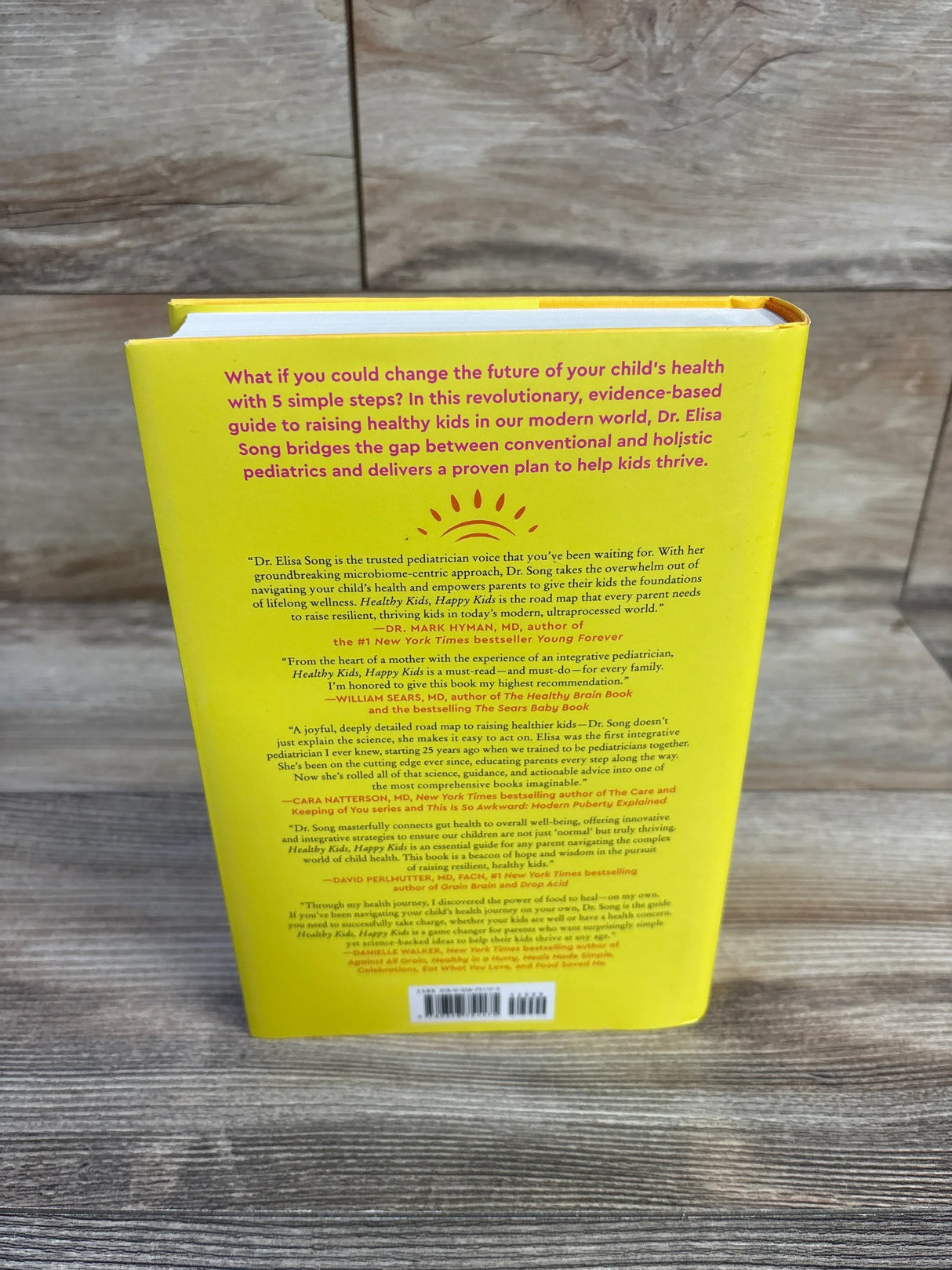 Back of Healthy Kids, Happy Kids hardcover book showing yellow cover with synopsis text and sun graphic on wood surface