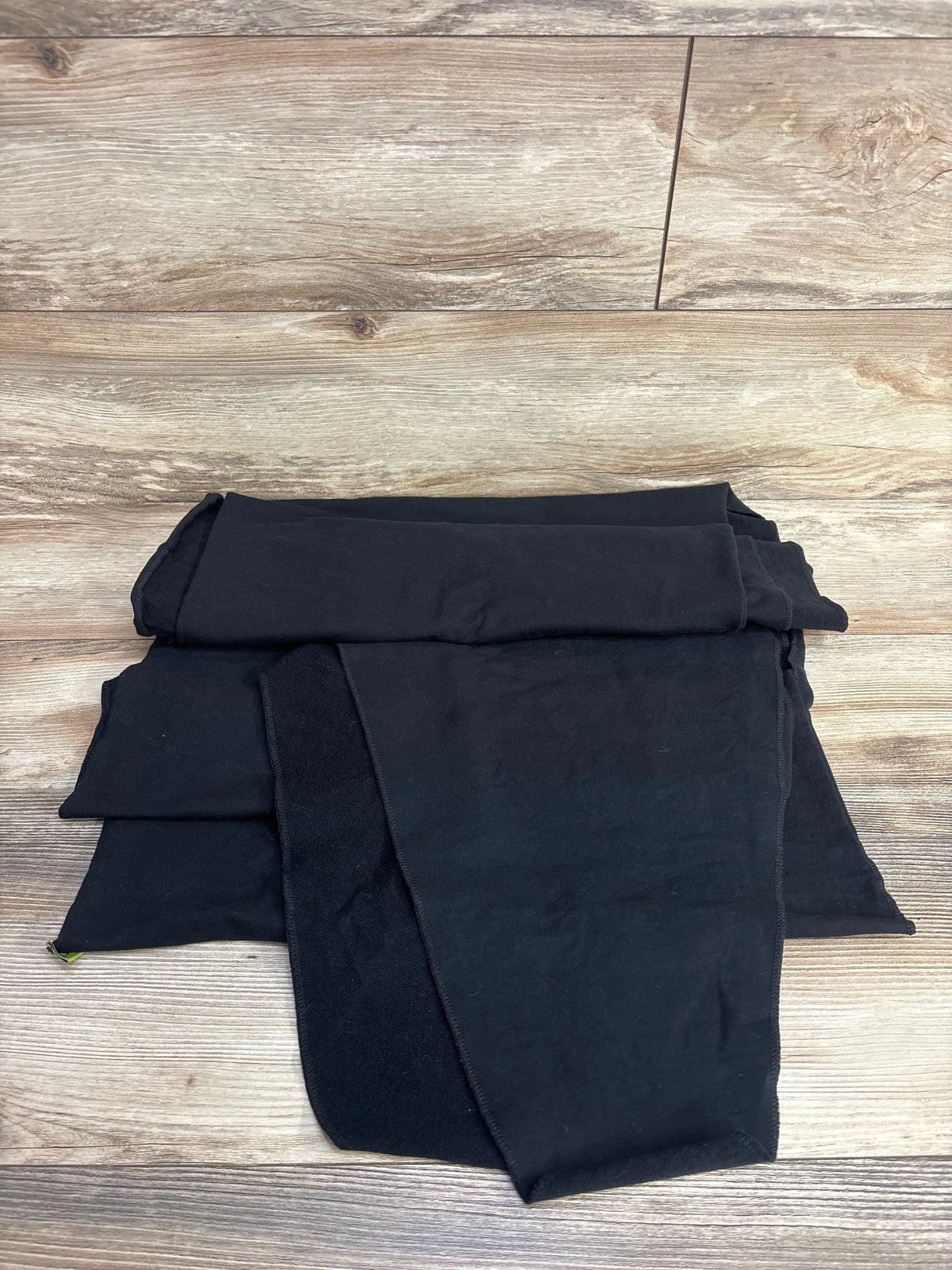 Folded Boba Classic baby wrap in black (7-35 lbs) showing long soft knit panels on a wood floor background