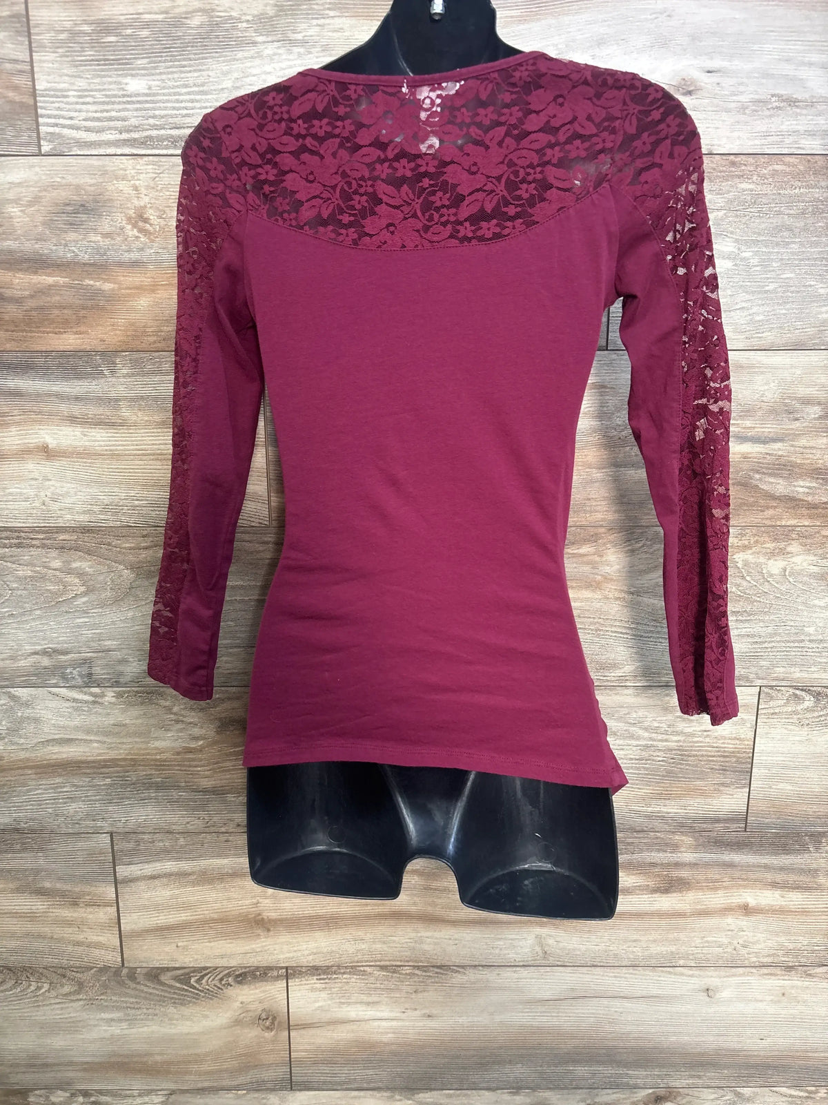 Back view of maroon maternity long sleeve shirt with floral lace yoke and lace sleeves on black mannequin, wood background