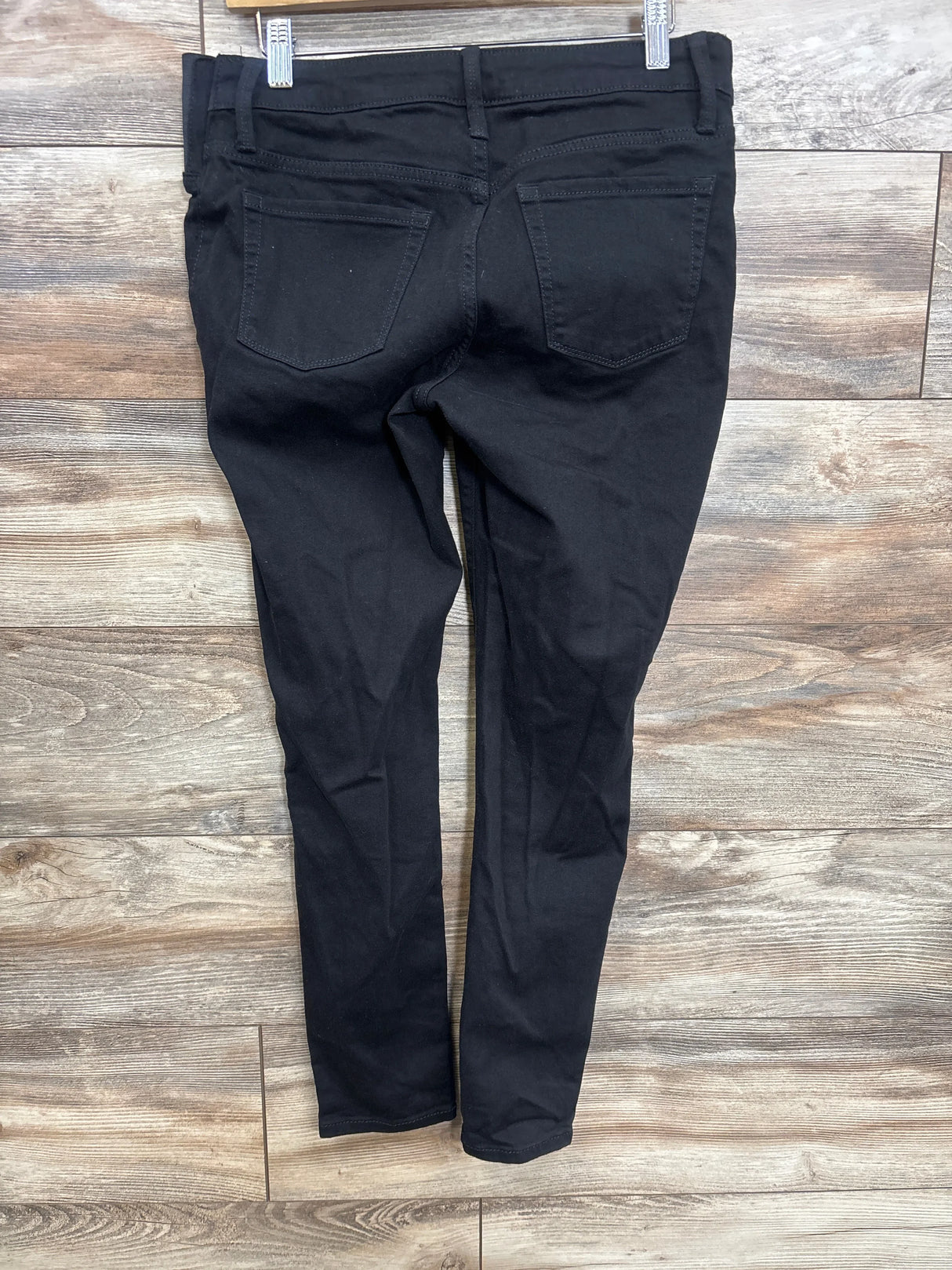 Back view of black Isabel maternity side-panel skinny jeans showcasing back pockets and slim tapered legs with a wood floor background