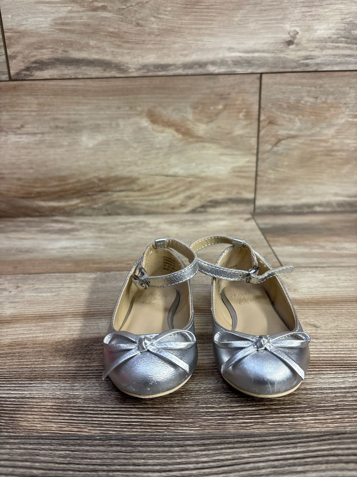 Pair of silver toddler girls' dress shoes with ankle straps and bows on wooden floor