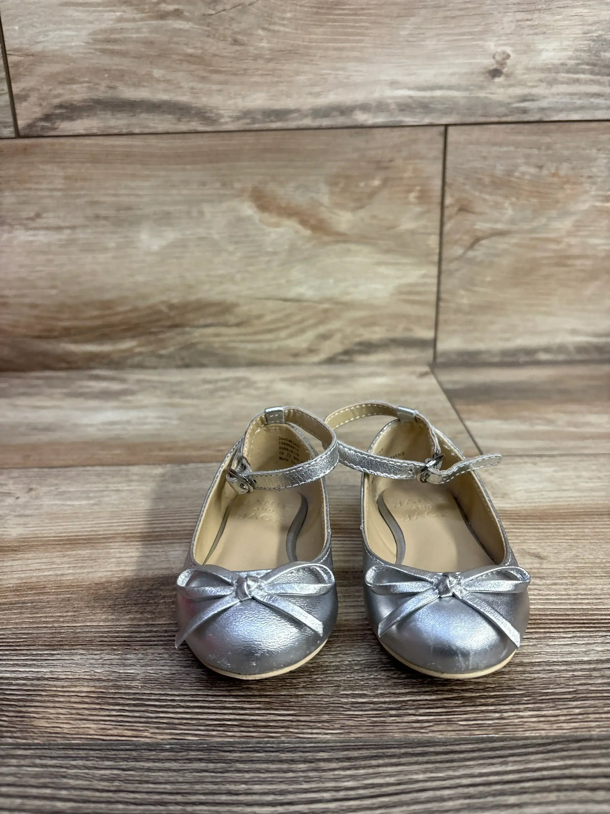Pair of silver toddler girls' dress shoes with ankle straps and bows on wooden floor