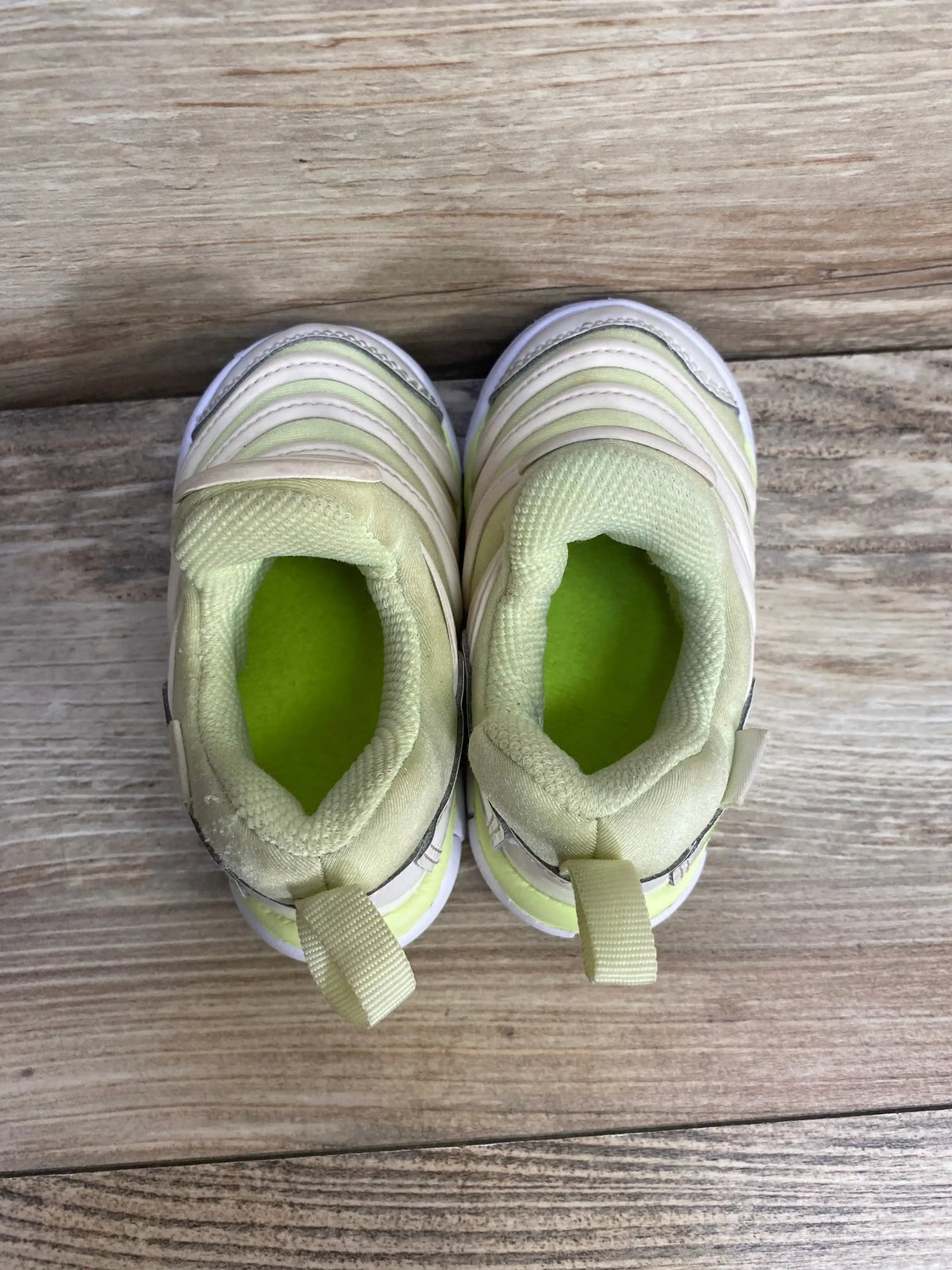 Top view of Nike Dynamo Free toddler sneakers, size 5C, white with light green insoles, padded collar and heel pull tabs on wooden floor