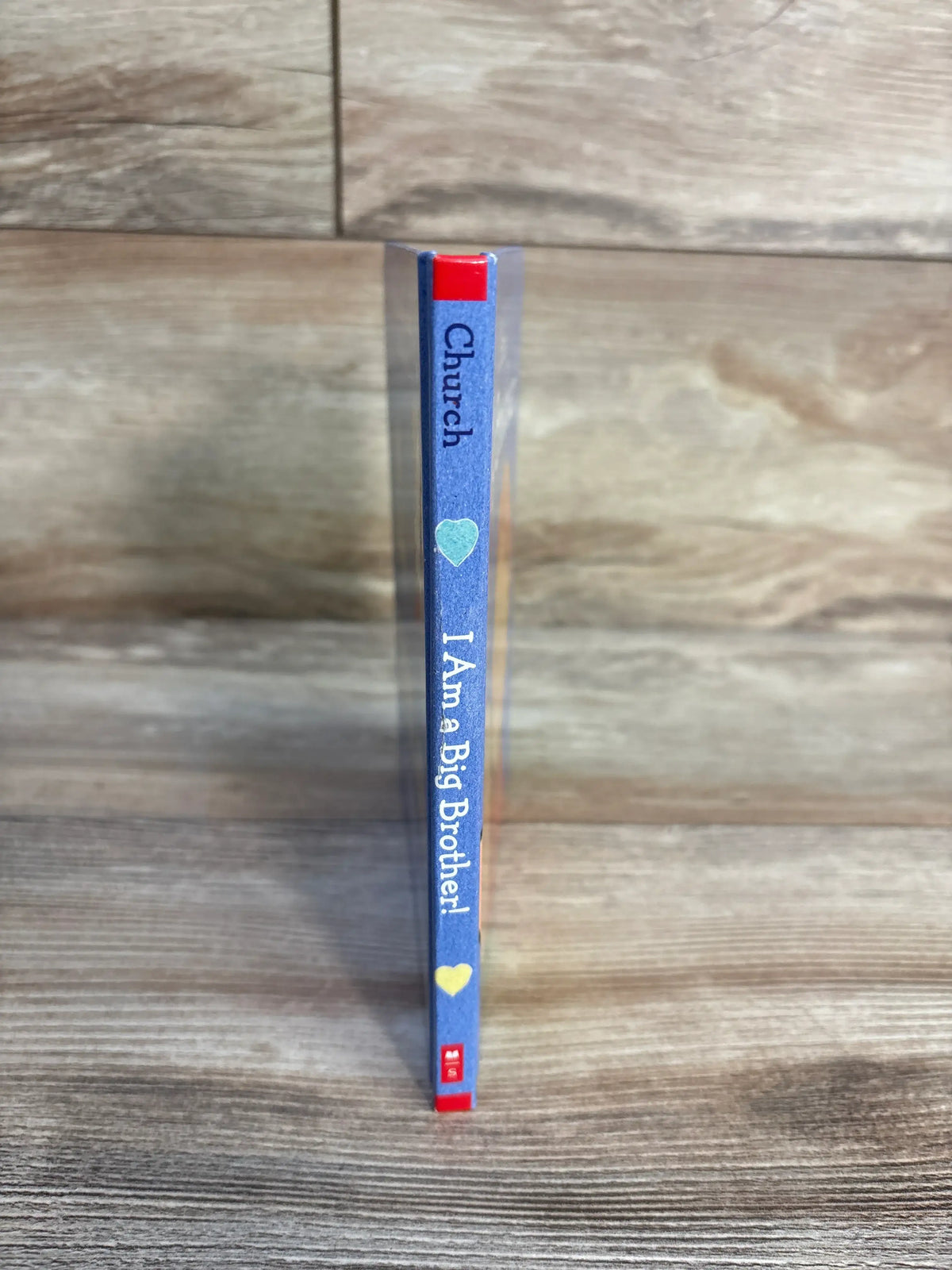 Spine view of I Am a Big Brother hardcover book showing blue cover, printed title, and heart icons on a wood-grain background