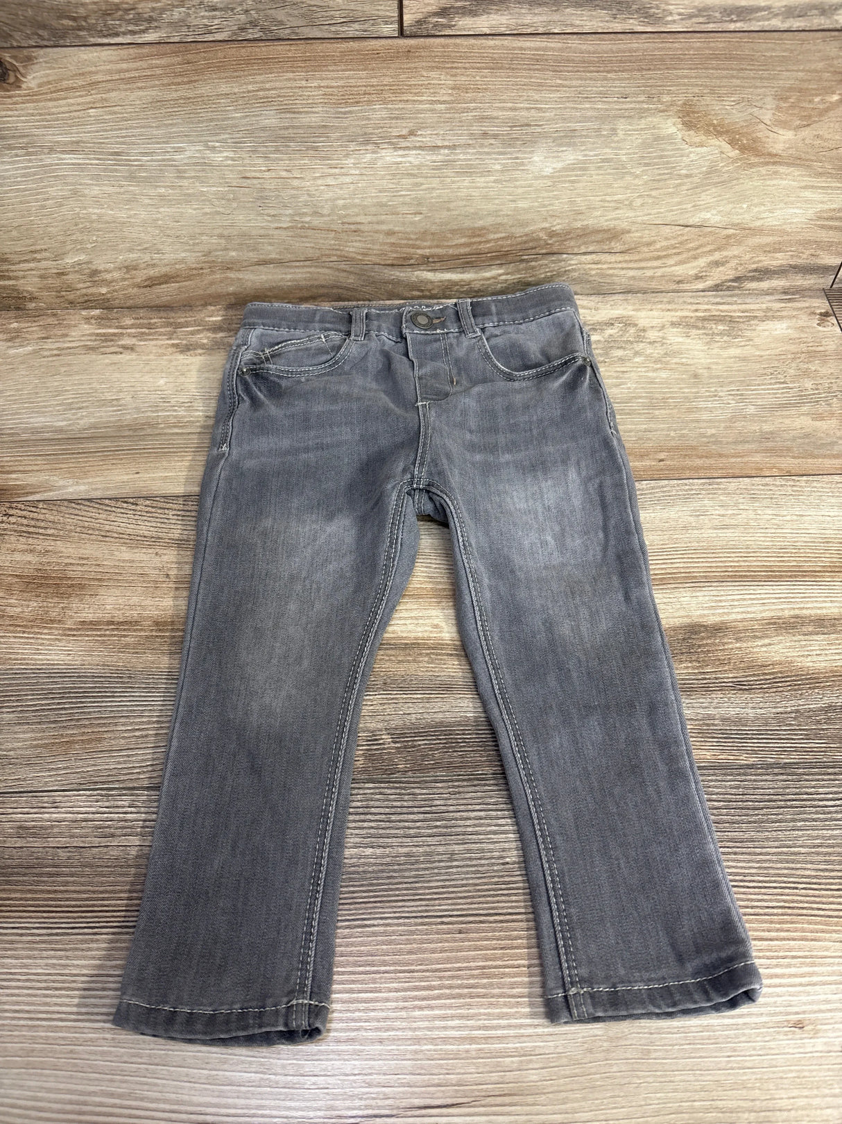 Gray denim kids jeans with front pockets and button, displayed on wood background